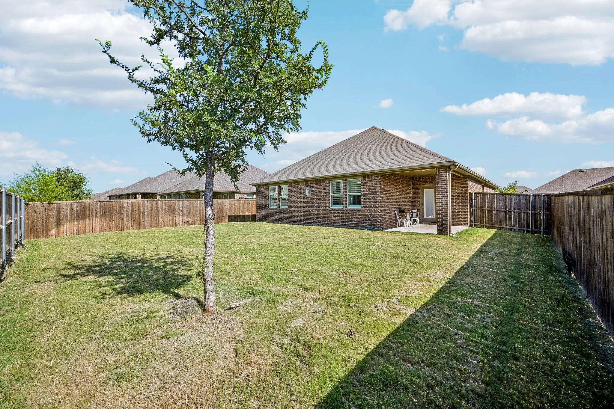 Spacious backyard featuring a covered patio, brick exterior, and a privacy fence