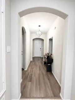 Hallway featuring wood-finish flooring, light-toned walls, arched doorways, a ceiling-mounted geometric light fixture, and white trim