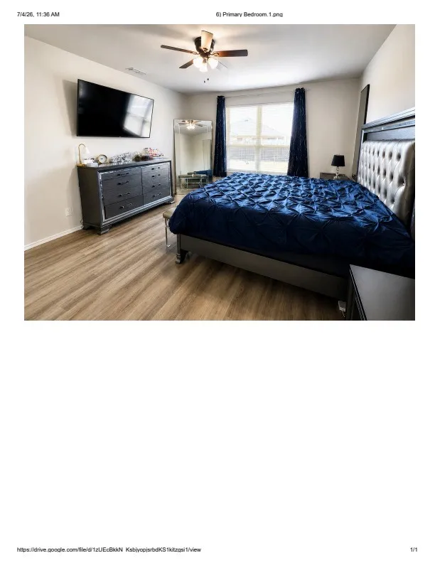 Spacious room featuring wood-finish flooring, a ceiling fan with integrated lighting, and a large window with privacy blinds