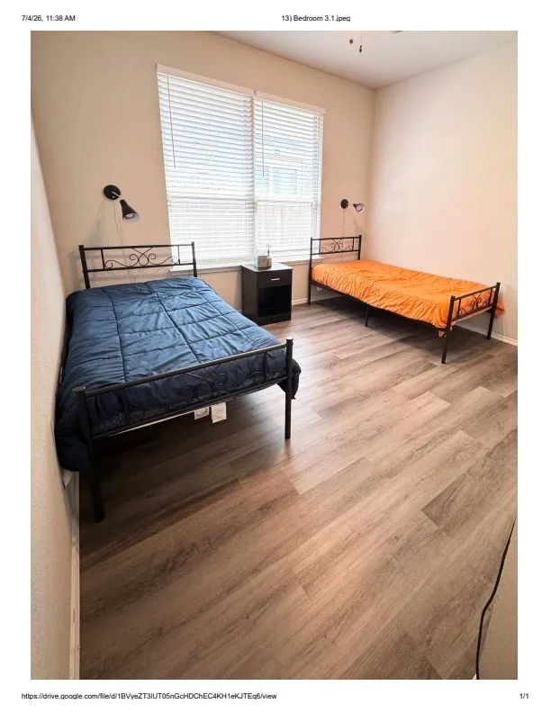 Bedroom featuring wood-finish flooring, neutral wall tones, a window with blinds, and two wall-mounted light fixtures