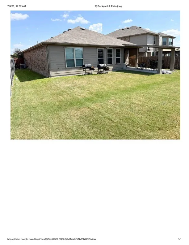 Expansive backyard featuring a covered patio, a manicured lawn, and multi-pane windows