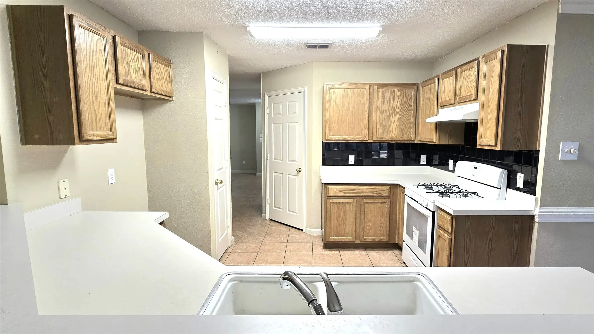 Kitchen featuring a built-in sink, wood-finish cabinetry, a white gas range, and black tile backsplash