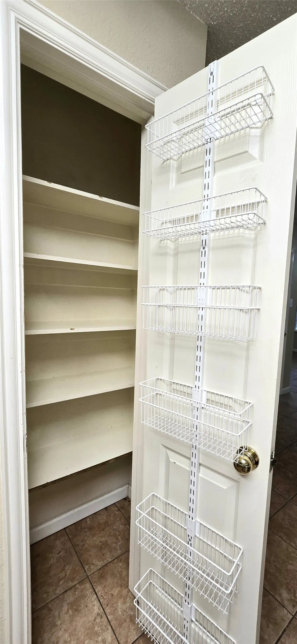 Built-in shelving with multiple levels, over-the-door wire storage baskets, and ceramic tile flooring