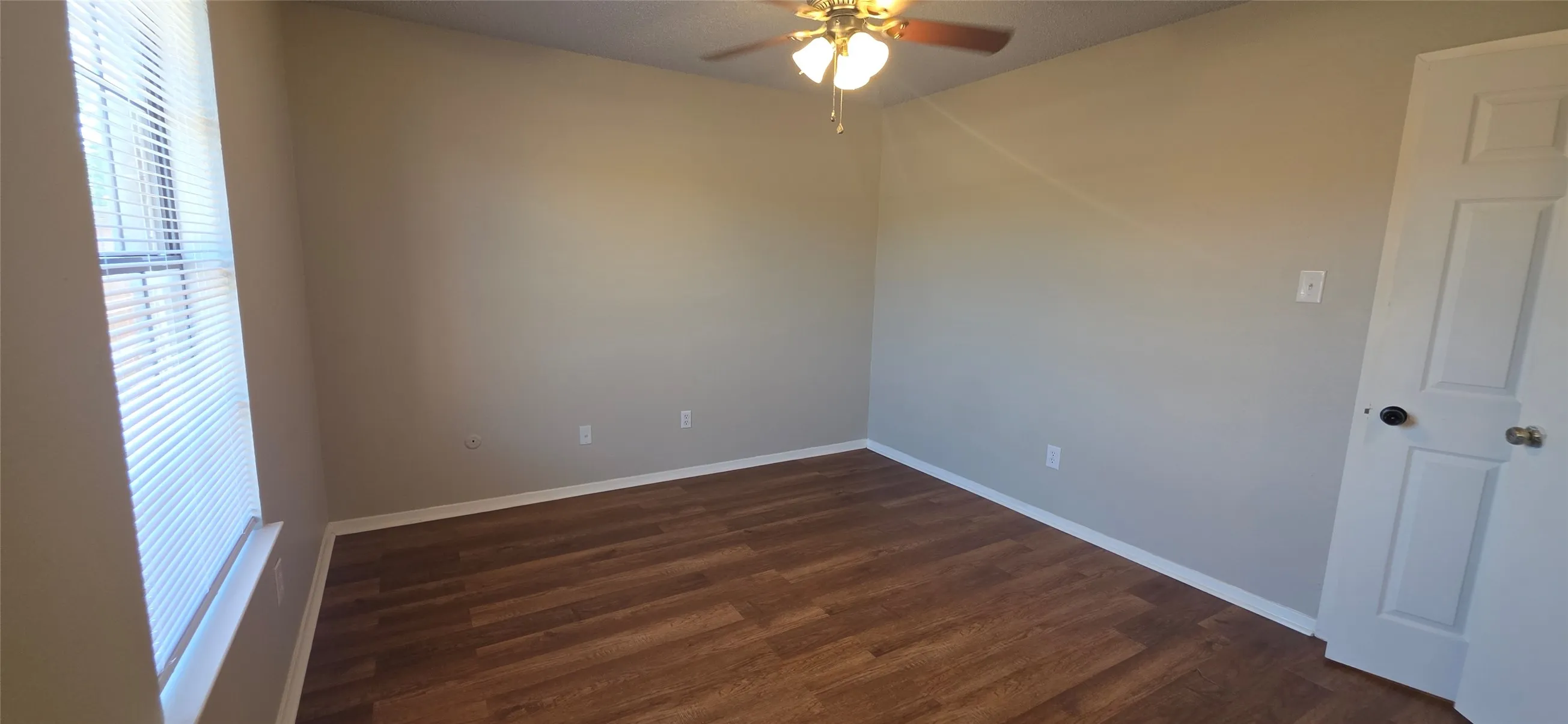 Room featuring wood-finish flooring, a ceiling fan with integrated lighting, and a paneled door