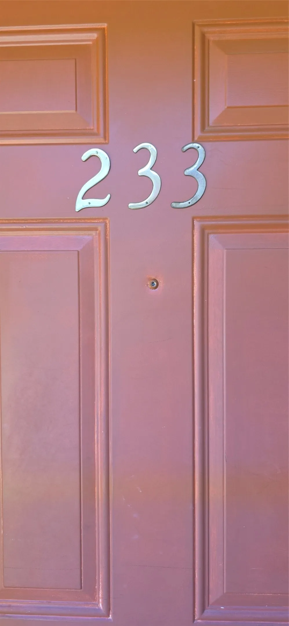 Panel-style entry door with a peephole and decorative house numbers
