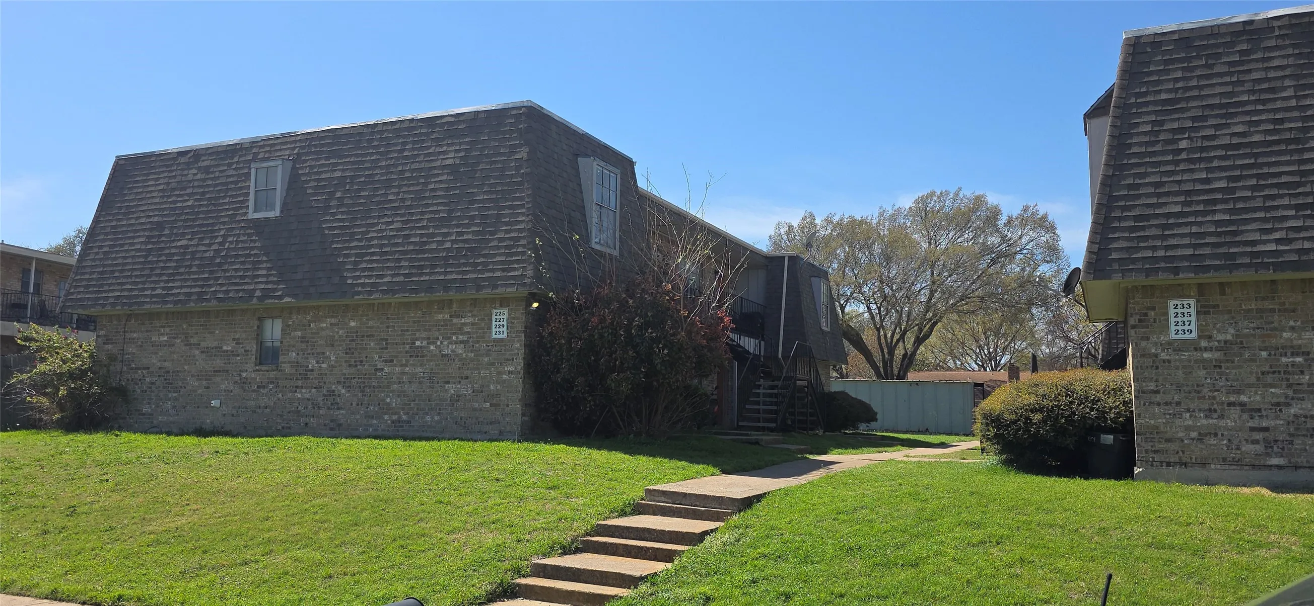 Brick exterior building featuring a mansard roof with dormer windows, a walkway with steps, and a grassy front yard