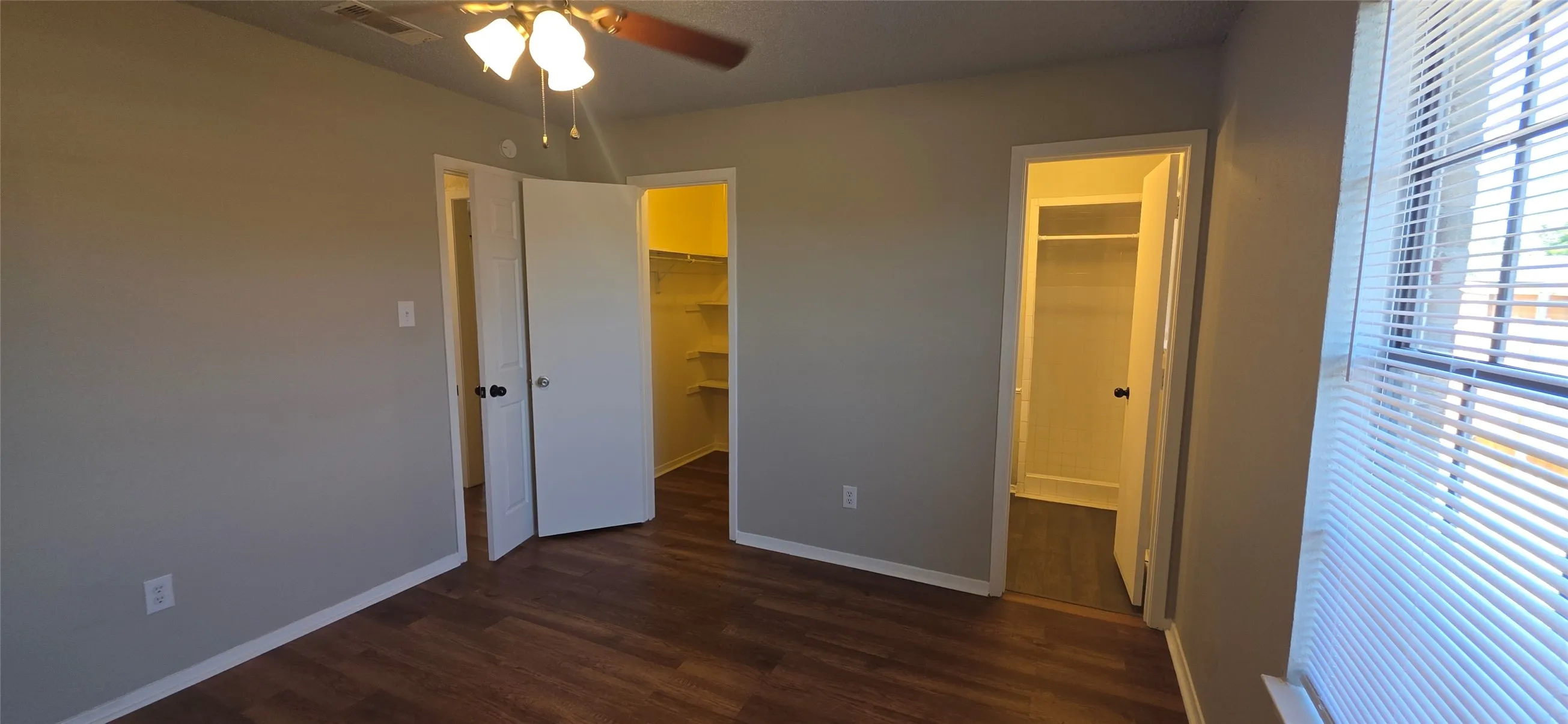Wood-finish flooring throughout, light neutral wall paint, ceiling fan with integrated lighting, and dual closet spaces