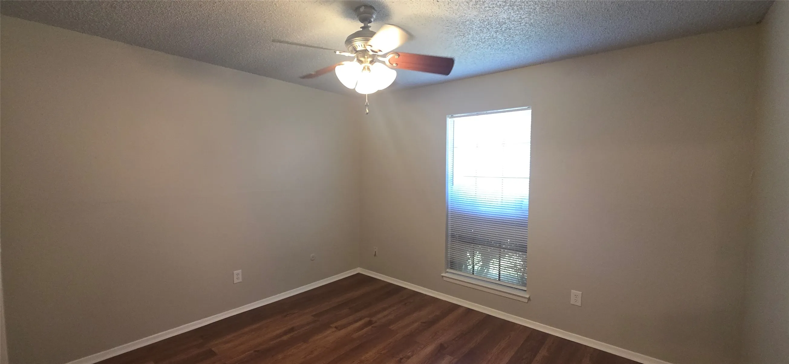 Wood-finish flooring, neutral wall tones, ceiling fan with integrated lighting, and a window providing natural illumination
