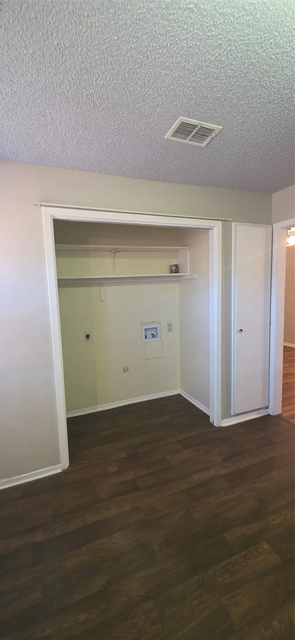 Laundry closet featuring hookups and a storage shelf, accompanied by wood-finish flooring and a white built-in cabinet