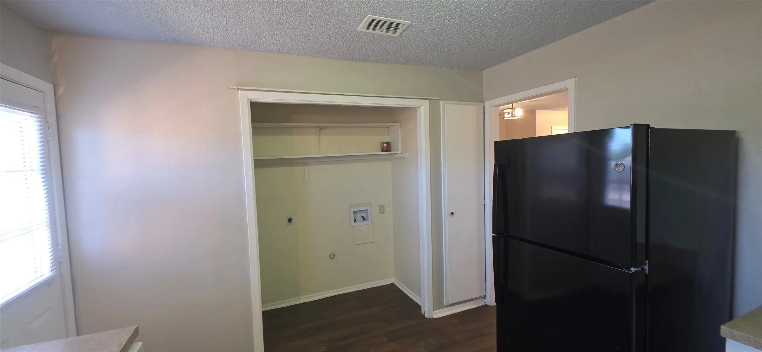Built-in laundry closet with shelving, wood-finish flooring, and a black refrigerator