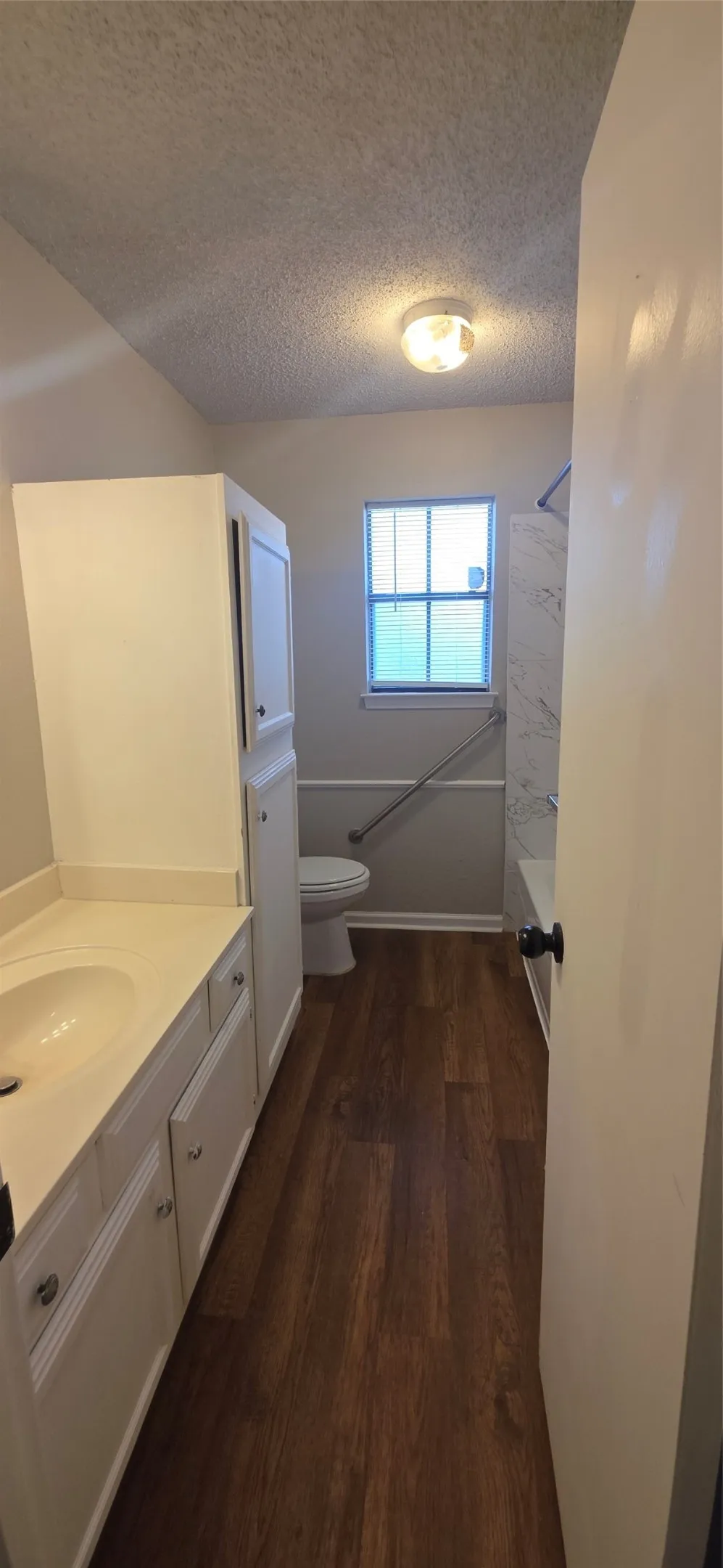 Wood-finish flooring, white vanity with integrated sink, white storage cabinetry, white toilet, and a tiled shower-tub combination