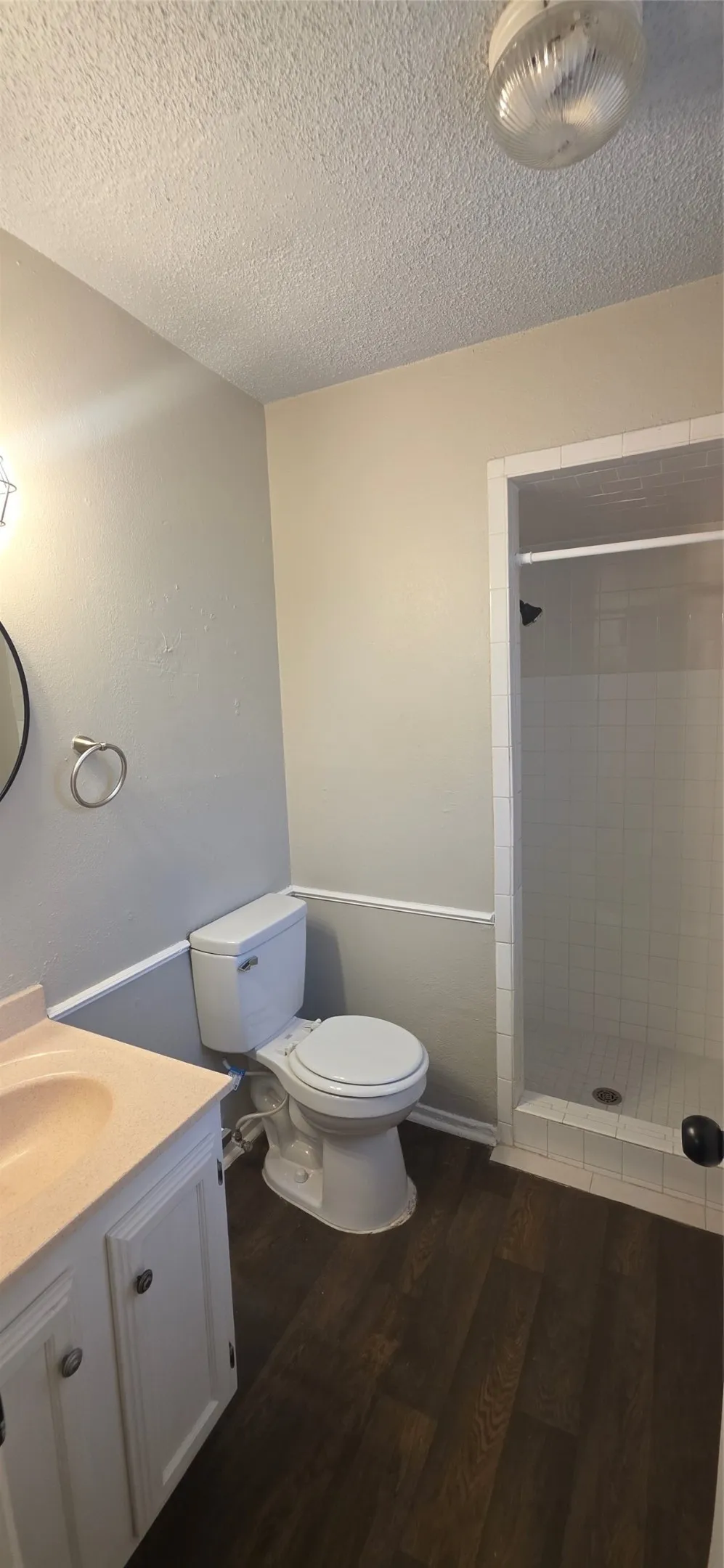 Bathroom featuring wood-finish flooring, white vanity with integrated sink, toilet, and a glass-enclosed shower