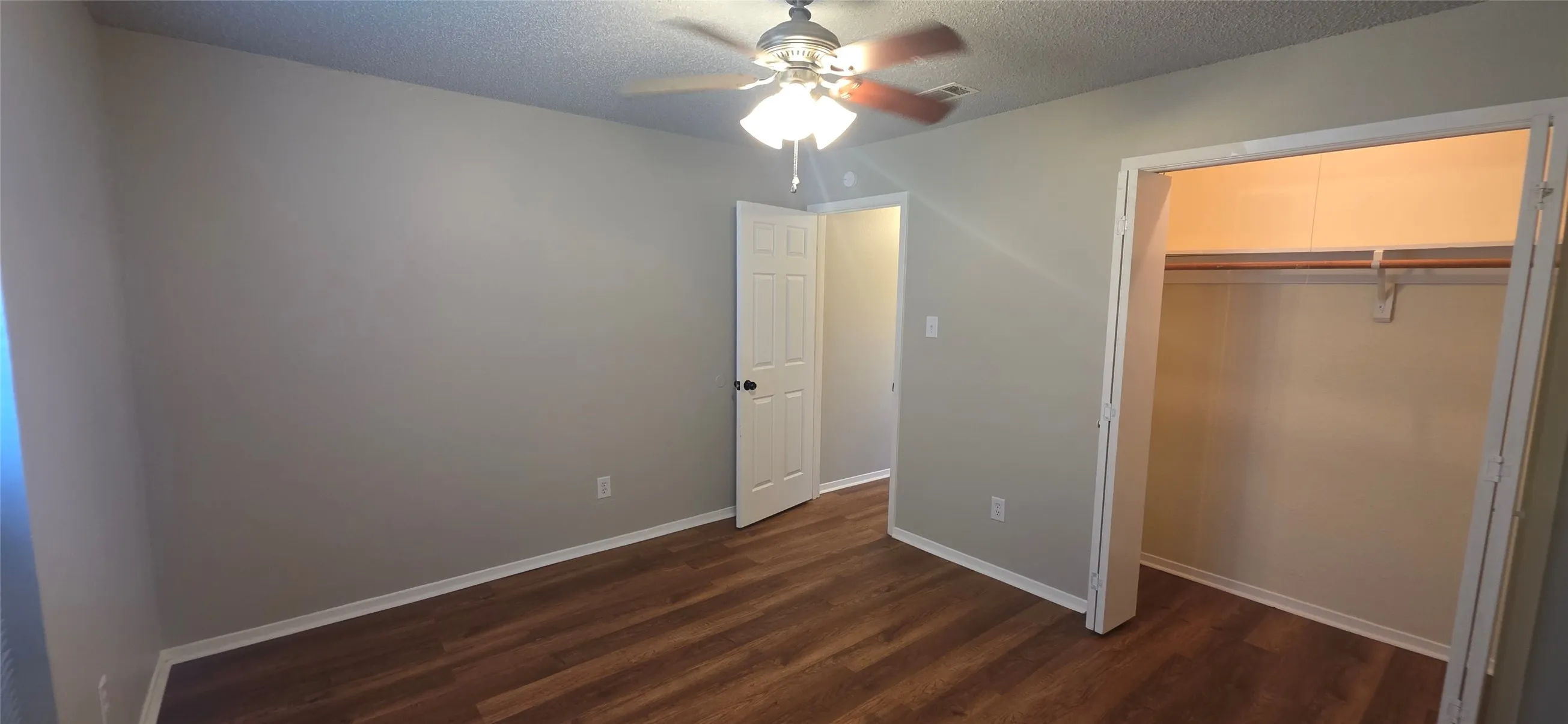 Room featuring wood-finish flooring, a ceiling fan with integrated lighting, and a closet with a built-in rod