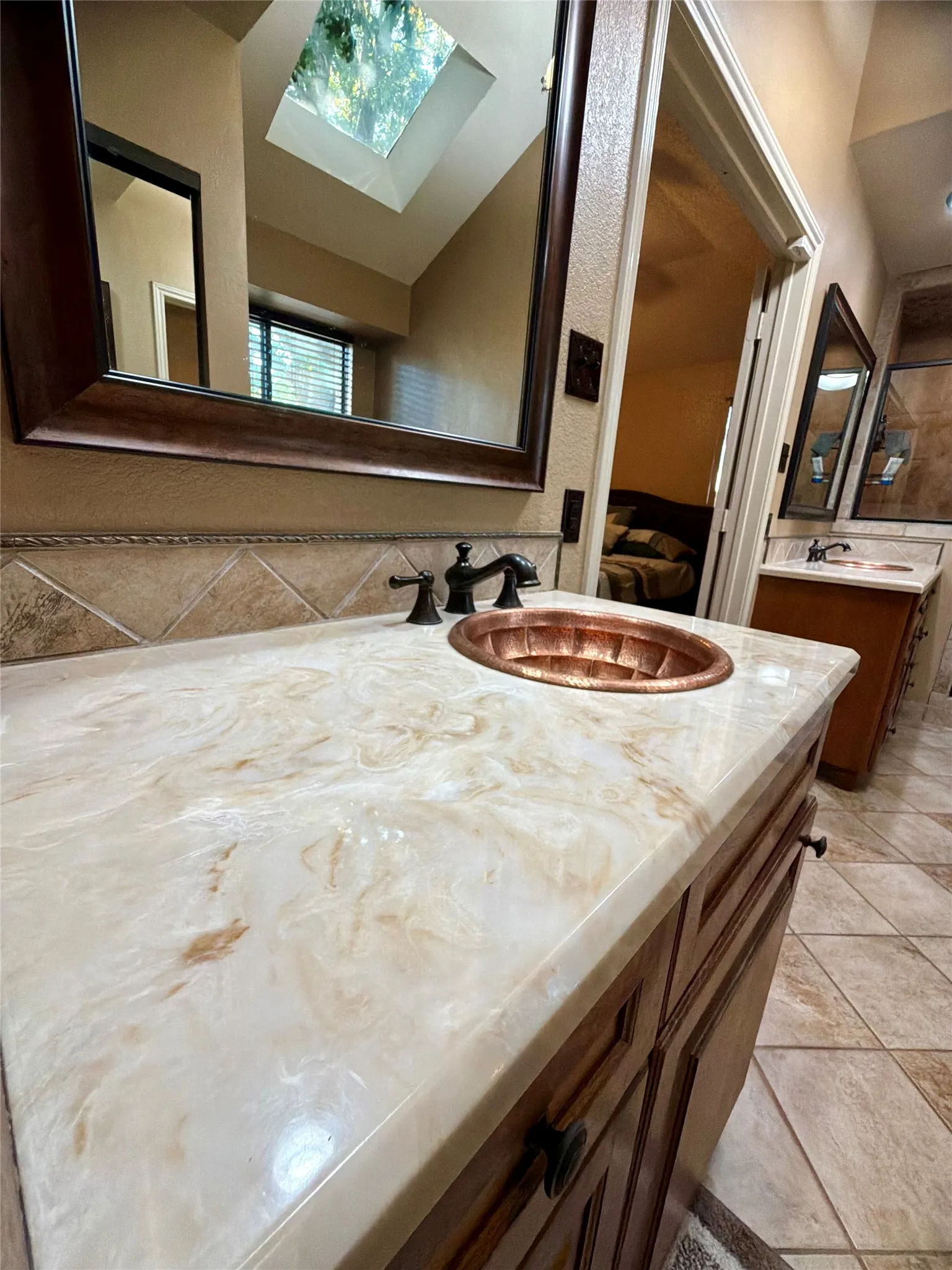 Vanity with a patterned countertop, copper vessel sink, dark bronze faucet, and wood-finish cabinetry