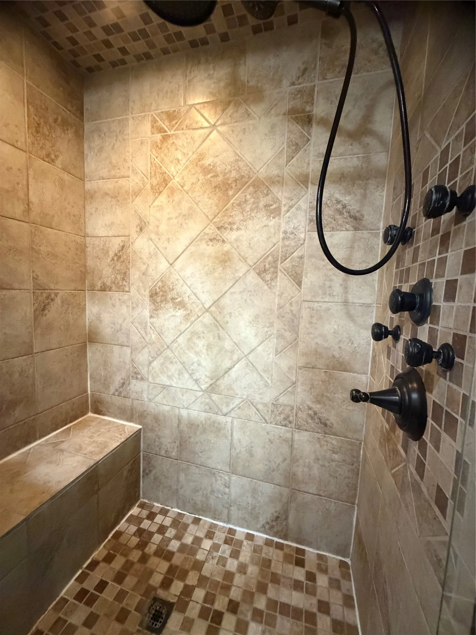 Tiled shower featuring a built-in bench, mosaic tile accents, and dark bronze fixtures