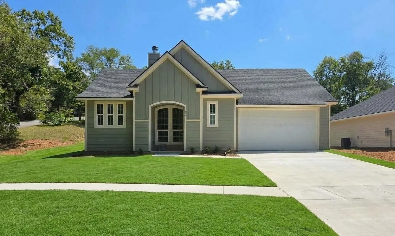 Exterior featuring light green siding with white trim, an arched entry door, a two-car garage, and a concrete driveway