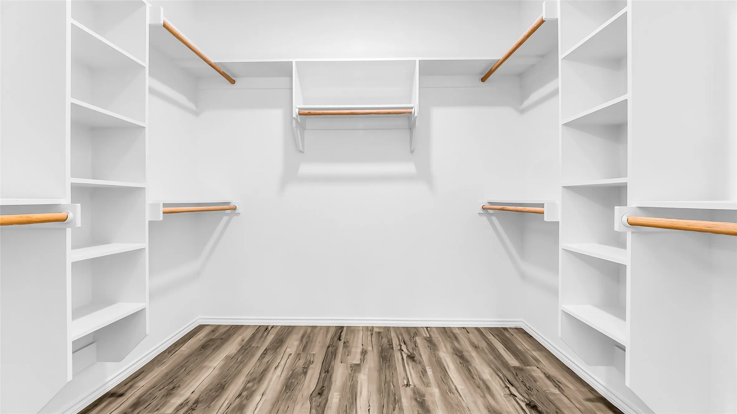 Built-in closet organization system with multiple shelving units, hanging rods, and wood-finish flooring