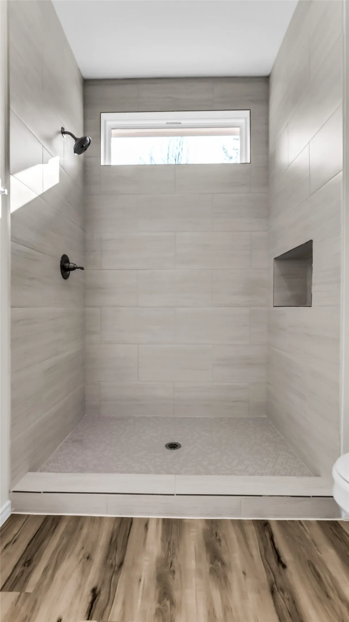 Walk-in shower with light gray tile surround, integrated shower niche, and a transom window