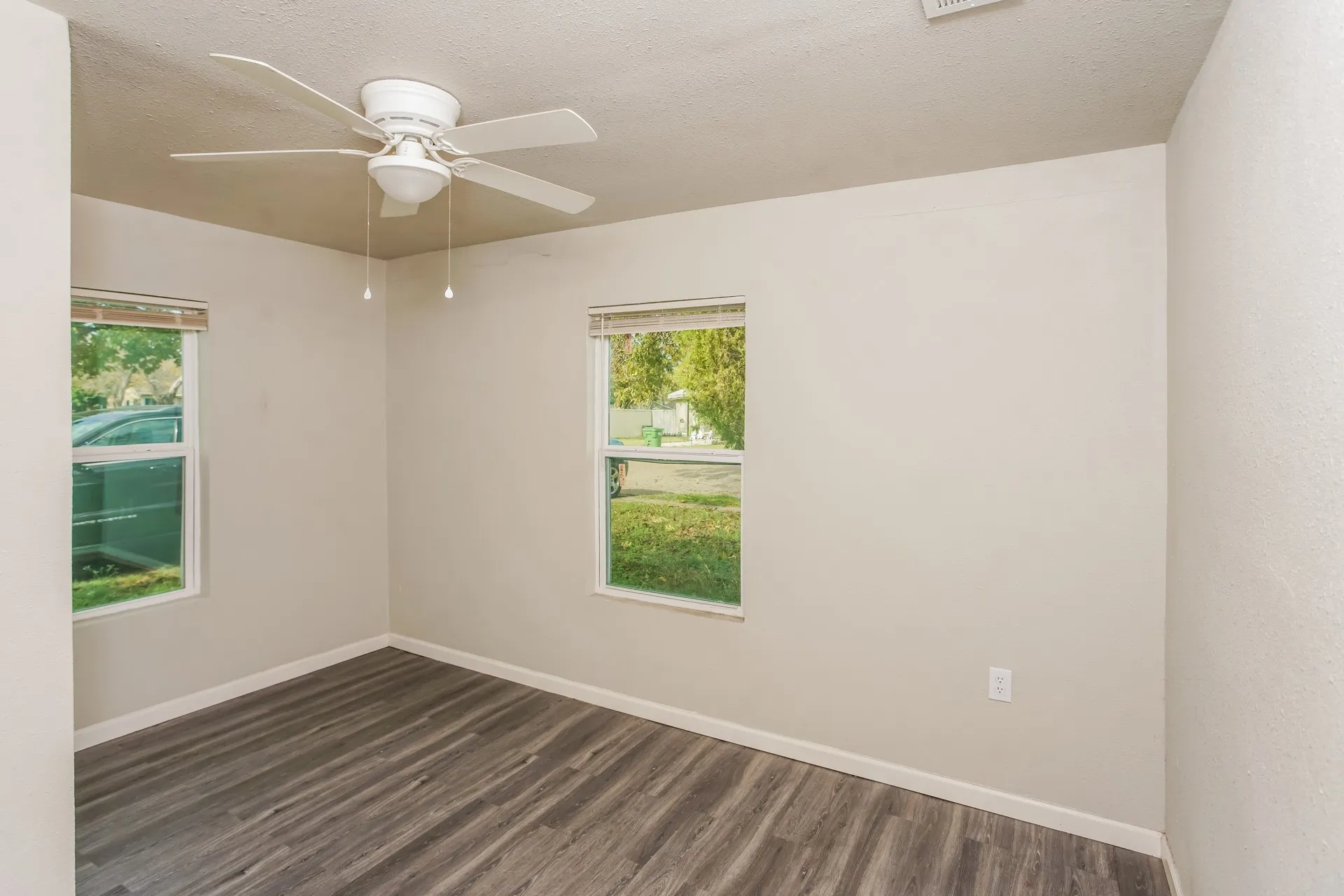 Room featuring wood-finish flooring, two windows with blinds, a white ceiling fan with integrated lighting, and neutral-toned walls