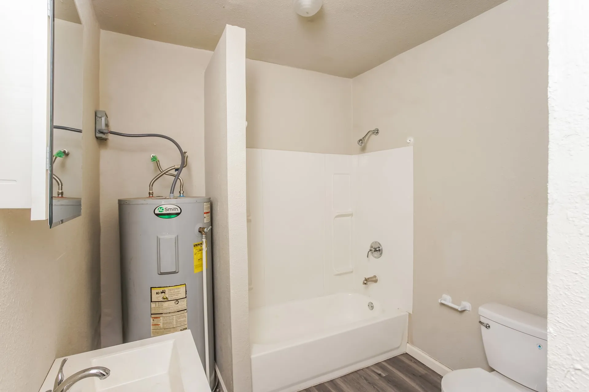 Bathroom featuring a white shower-over-tub combination, a toilet, a sink with a chrome faucet, and wood-finish flooring