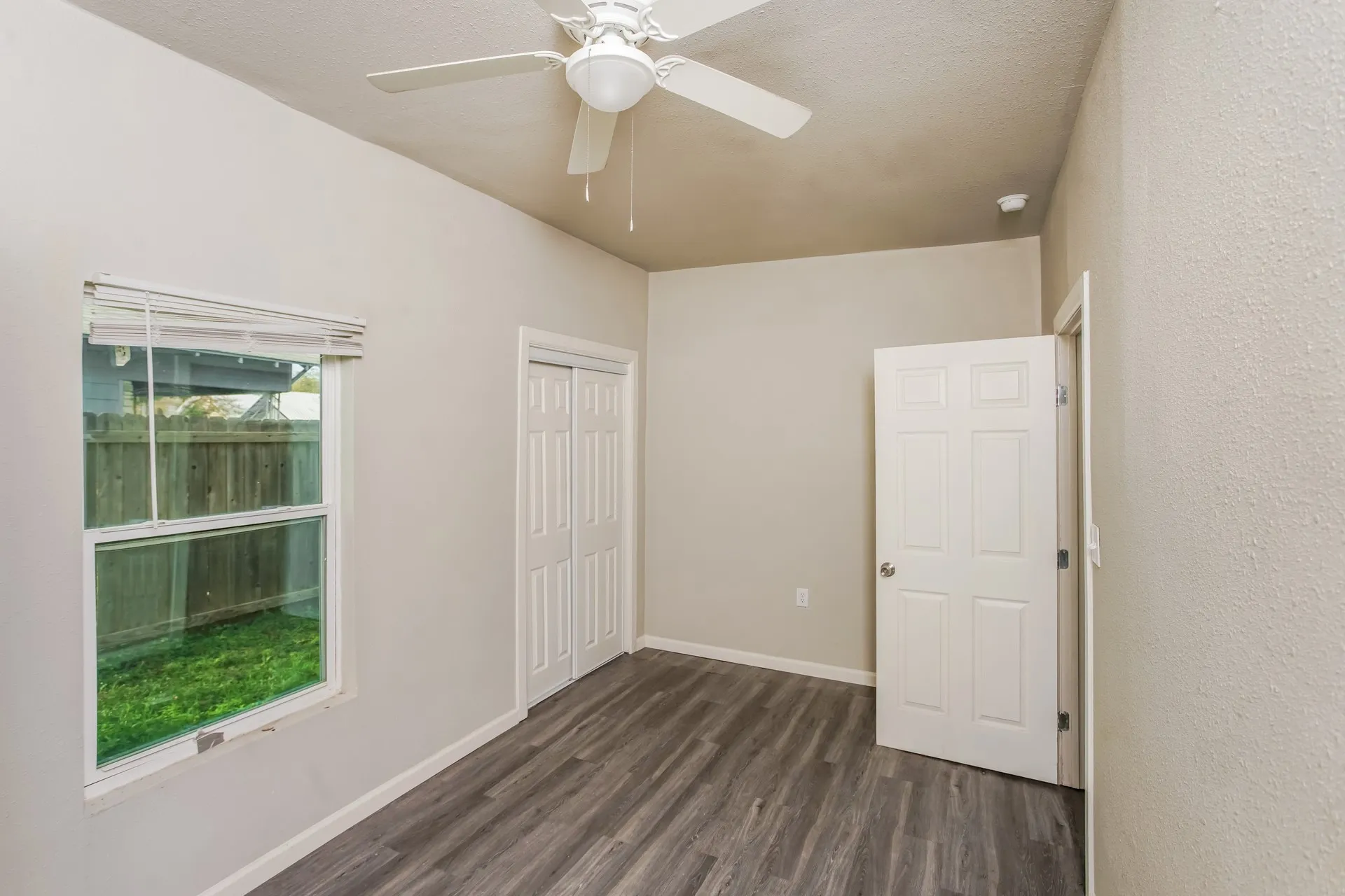 Room featuring wood-finish flooring, a ceiling fan with light fixture, a window providing natural illumination, bi-fold closet doors, and a six-panel door