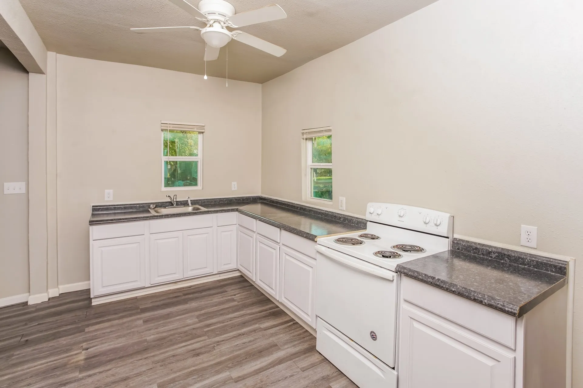 Kitchen area featuring wood-finish flooring, white cabinetry, dark countertops, a double basin sink, and a white electric range