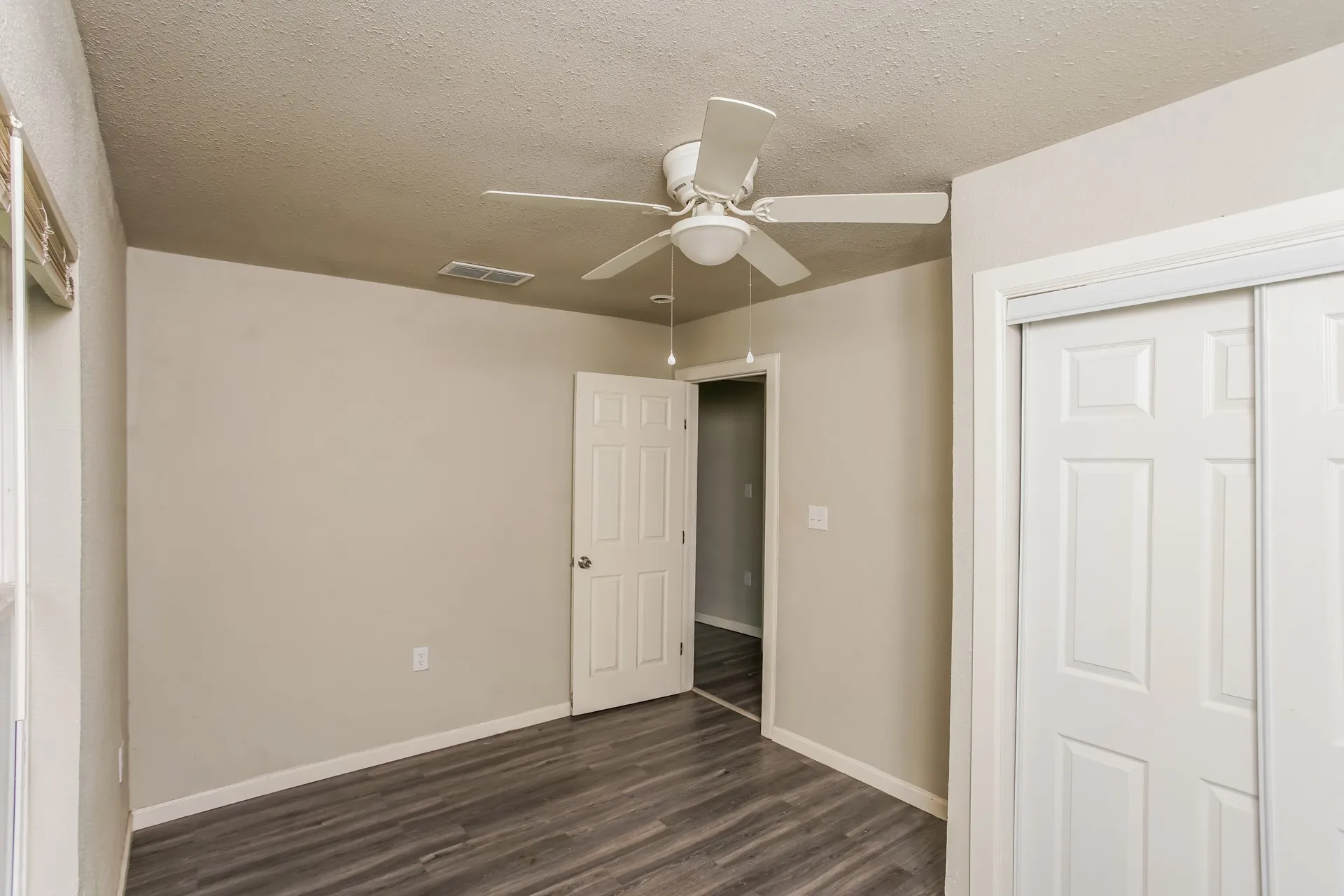 Room featuring wood-finish flooring, neutral wall paint, and a white ceiling fan with light kit