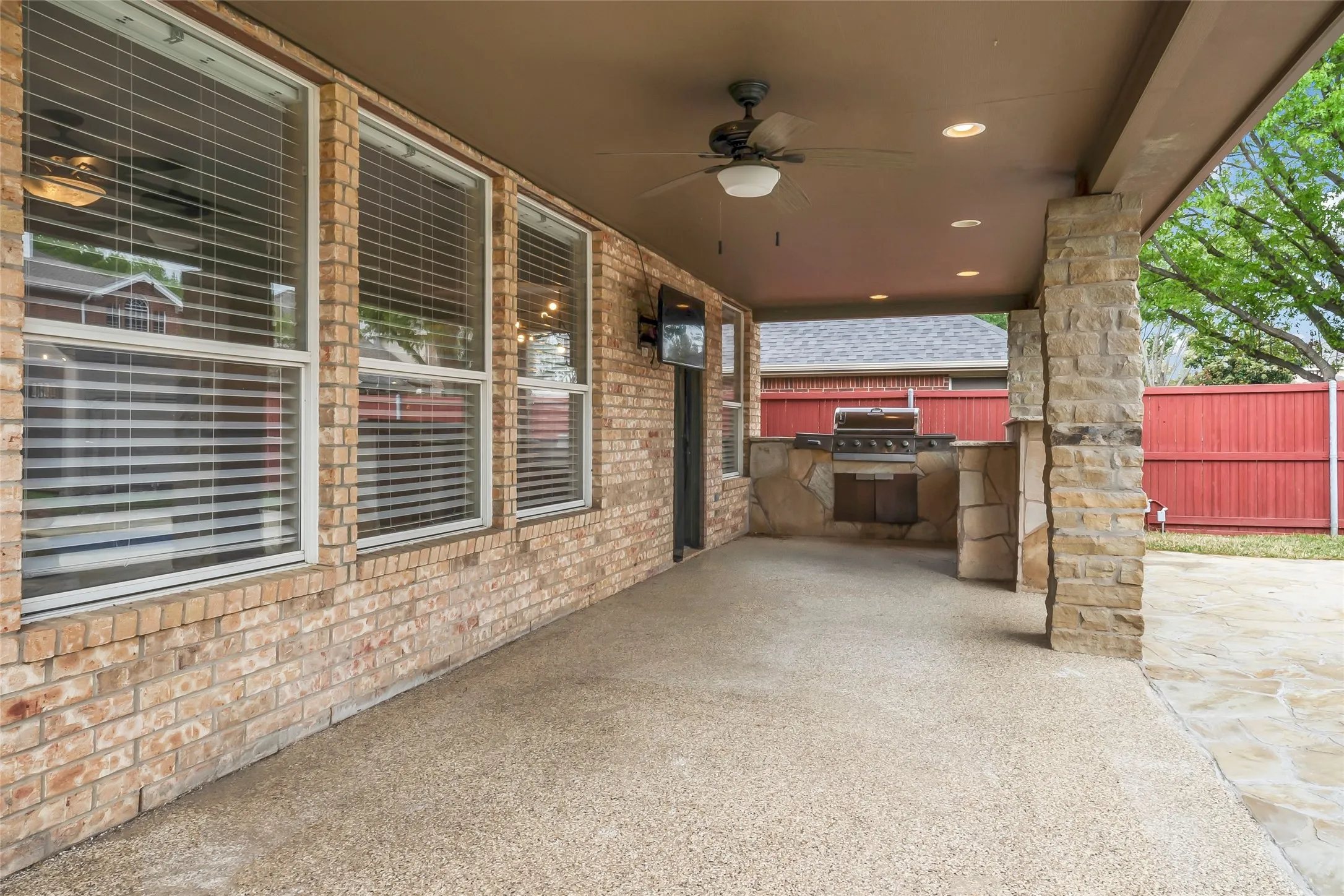 Covered patio featuring a built-in outdoor kitchen, ceiling fan, recessed lighting, and a stone accent column