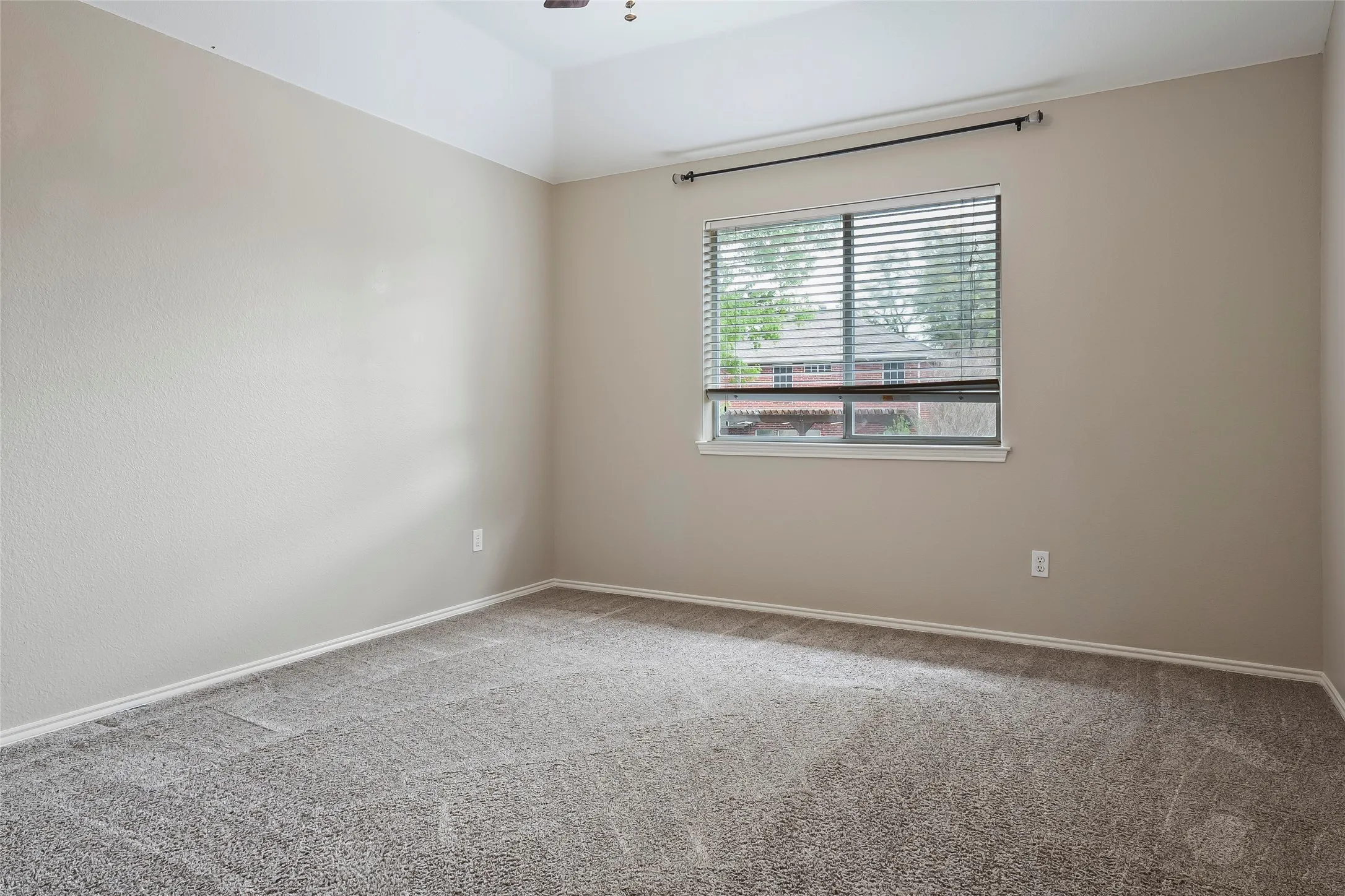 Carpeted room featuring a single window with horizontal blinds, neutral wall tones, white trim, and a tray ceiling