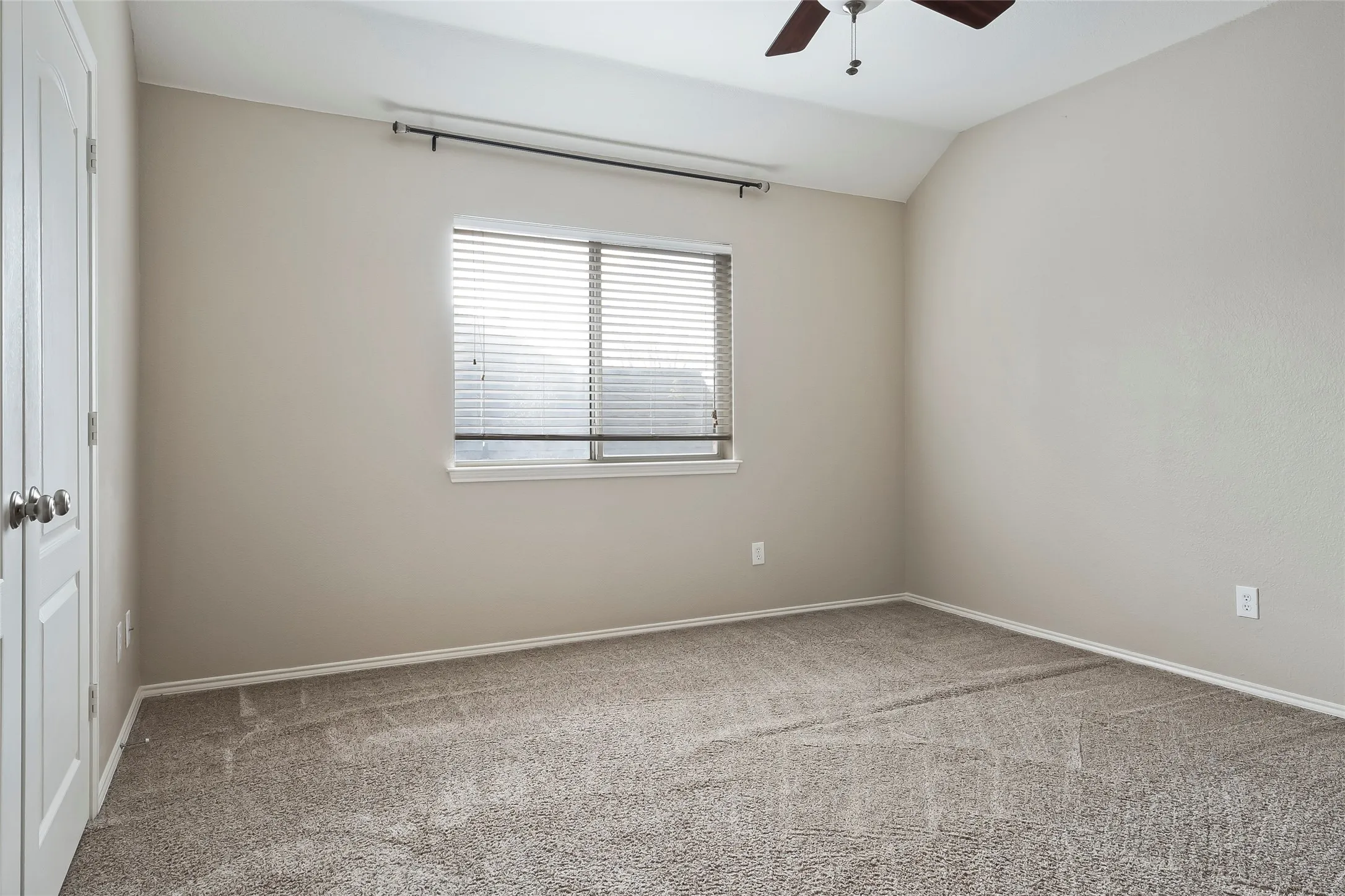 Room featuring neutral-toned walls, textured carpeting, and a window with blinds