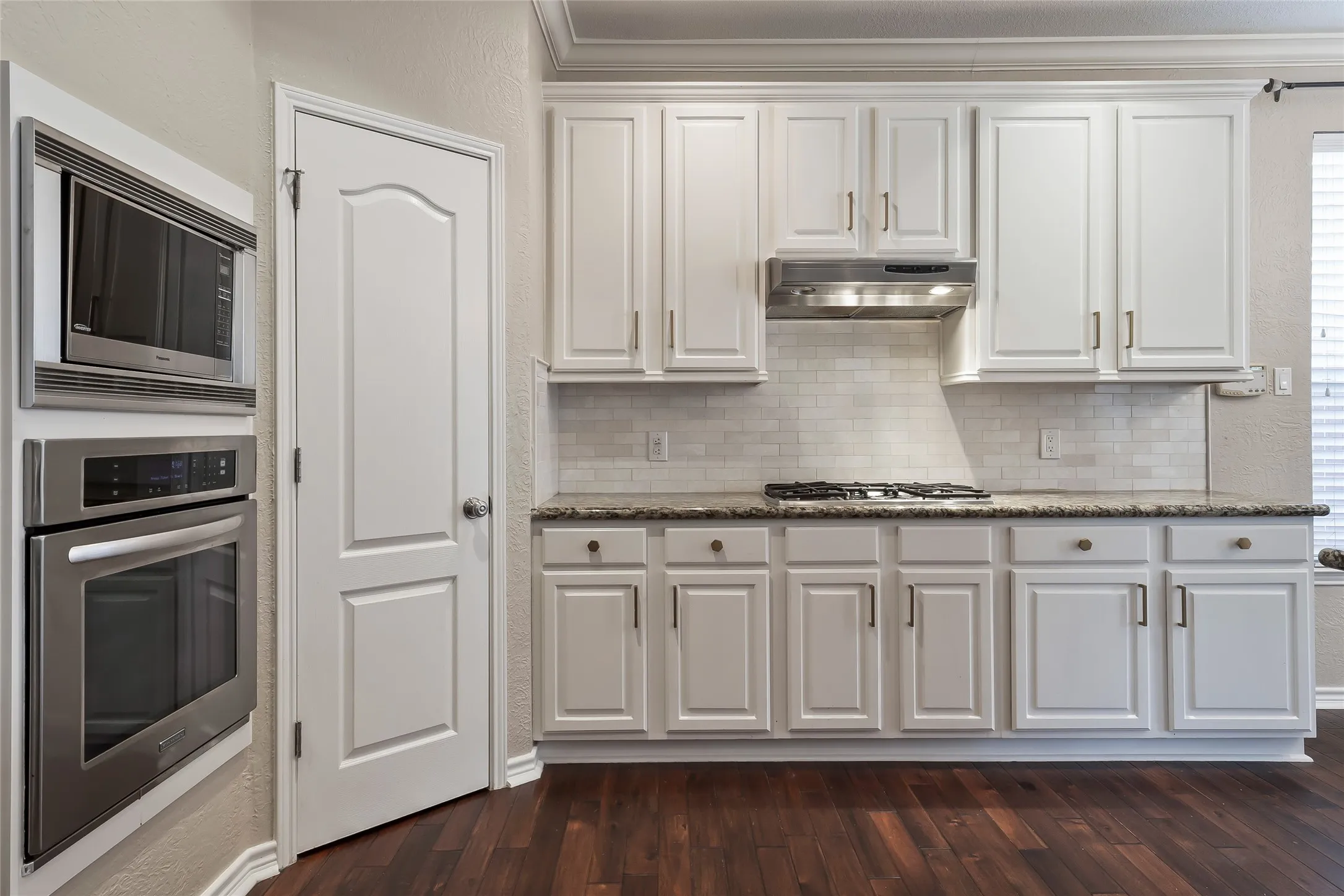 Kitchen featuring wood-finish flooring, white cabinetry, a built-in microwave, a wall oven, and a gas cooktop with a range hood