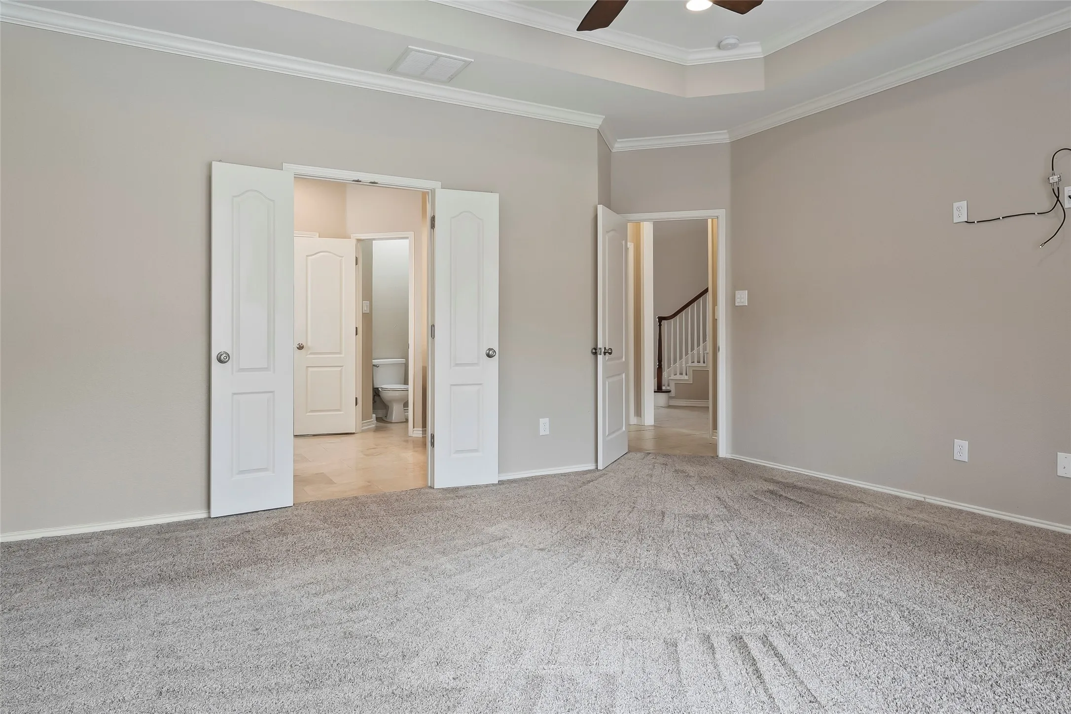 Spacious carpeted room featuring a tray ceiling with a ceiling fan, crown molding, and neutral wall paint
