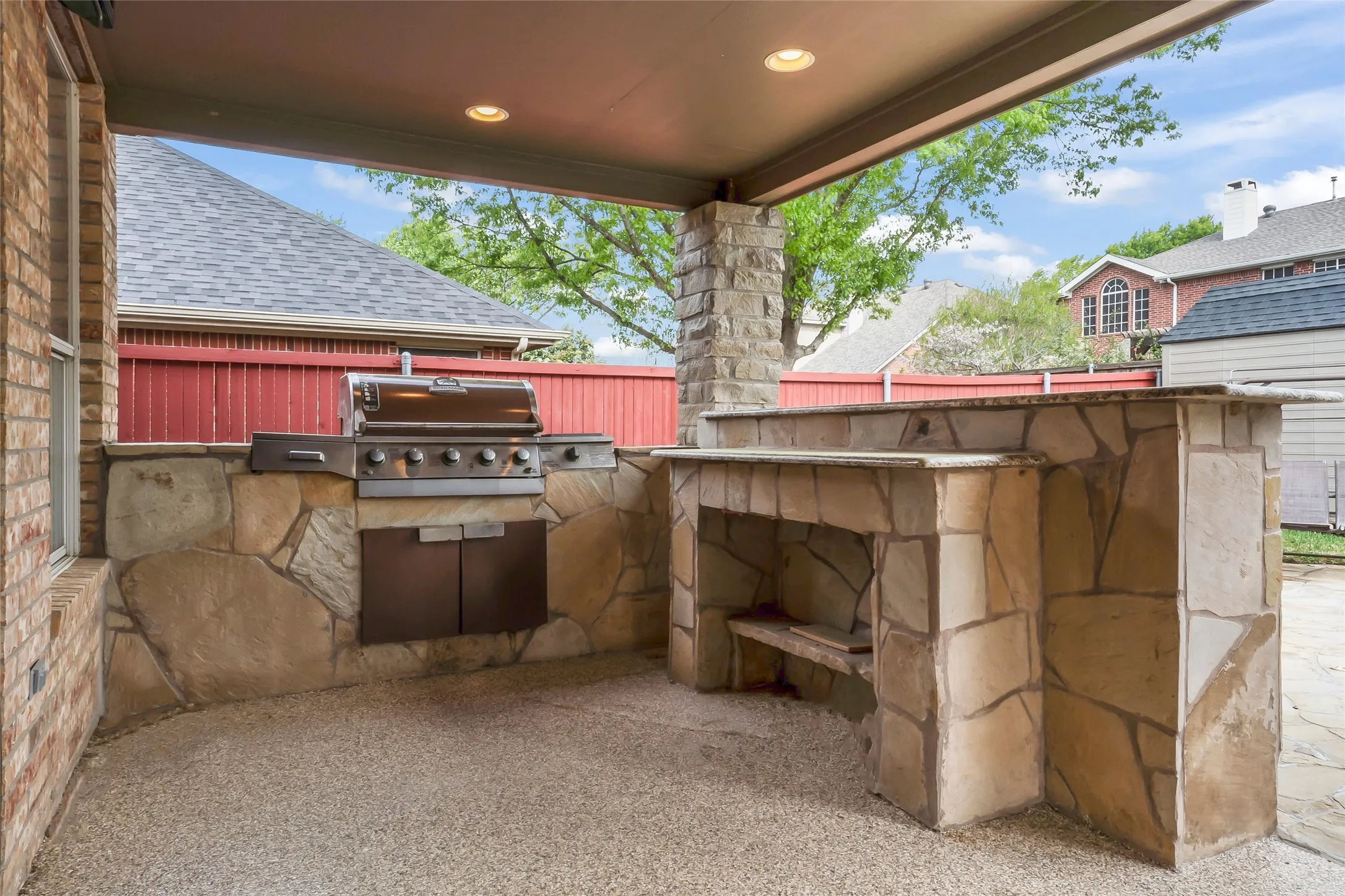 Covered patio featuring an outdoor kitchen with a built-in grill, stone veneer construction, and a bar-height countertop