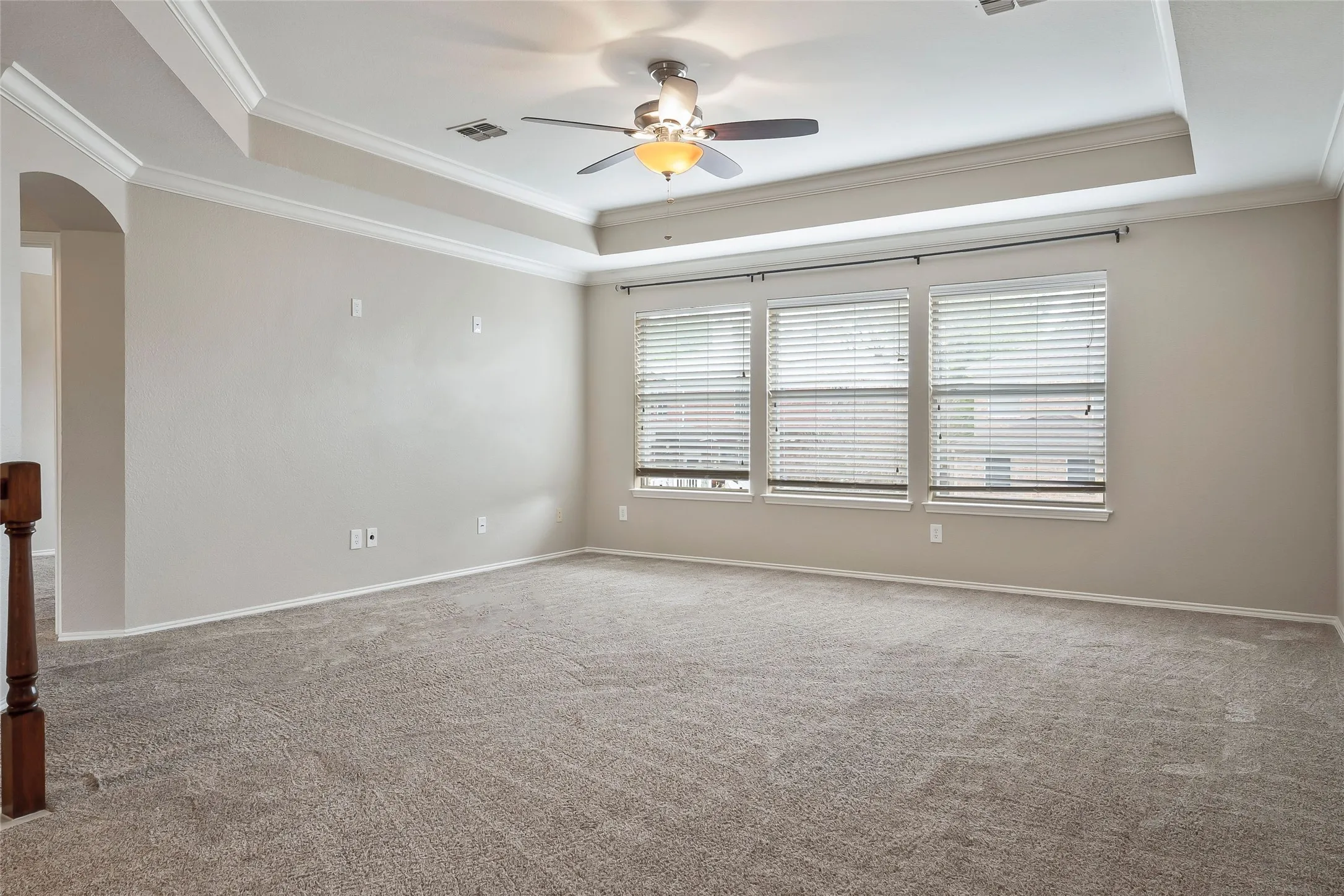 Spacious room featuring a tray ceiling with crown molding, a ceiling fan, and multiple windows with blinds