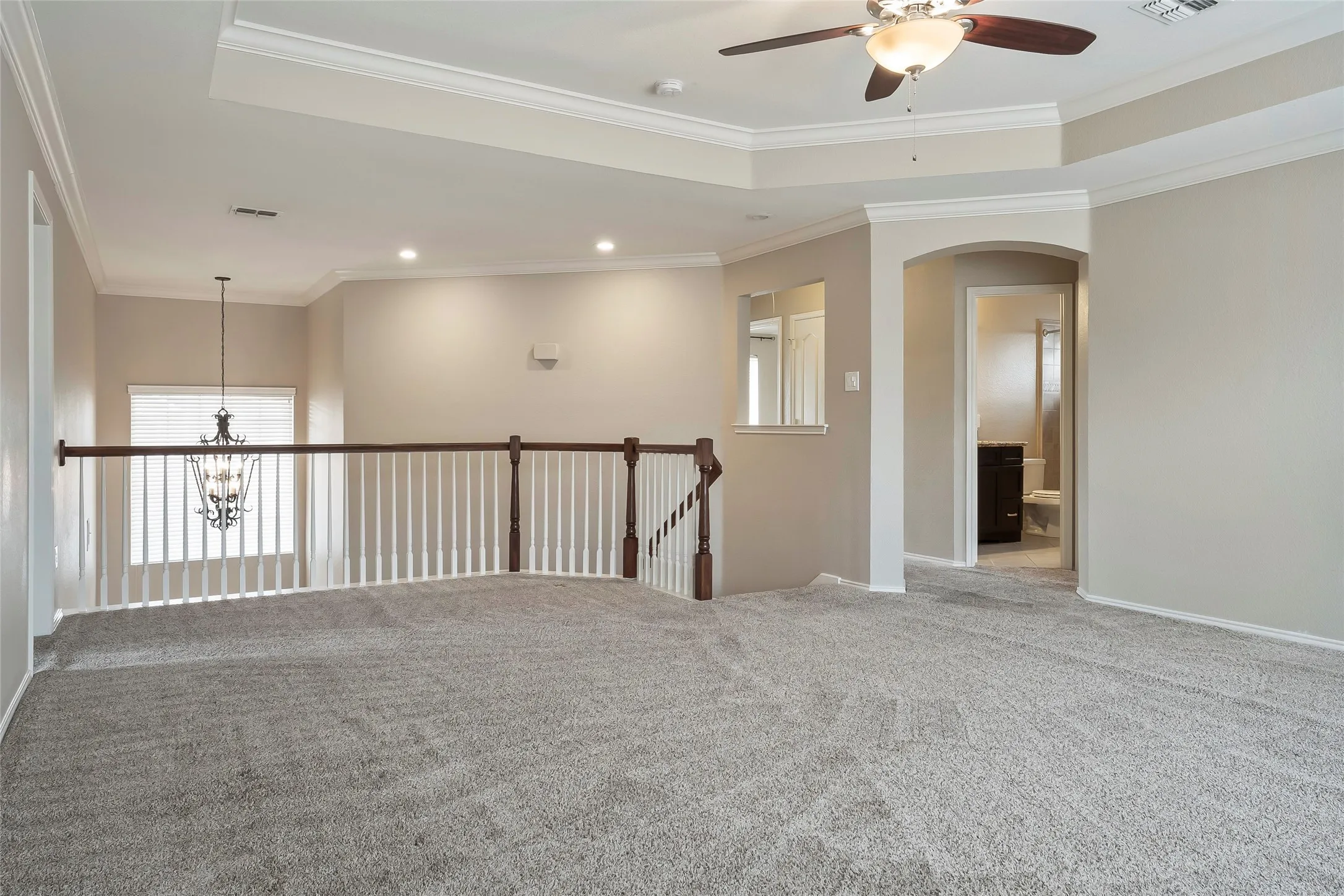 Spacious carpeted upper-level area featuring a tray ceiling with a fan light fixture, recessed lighting, and an arched doorway