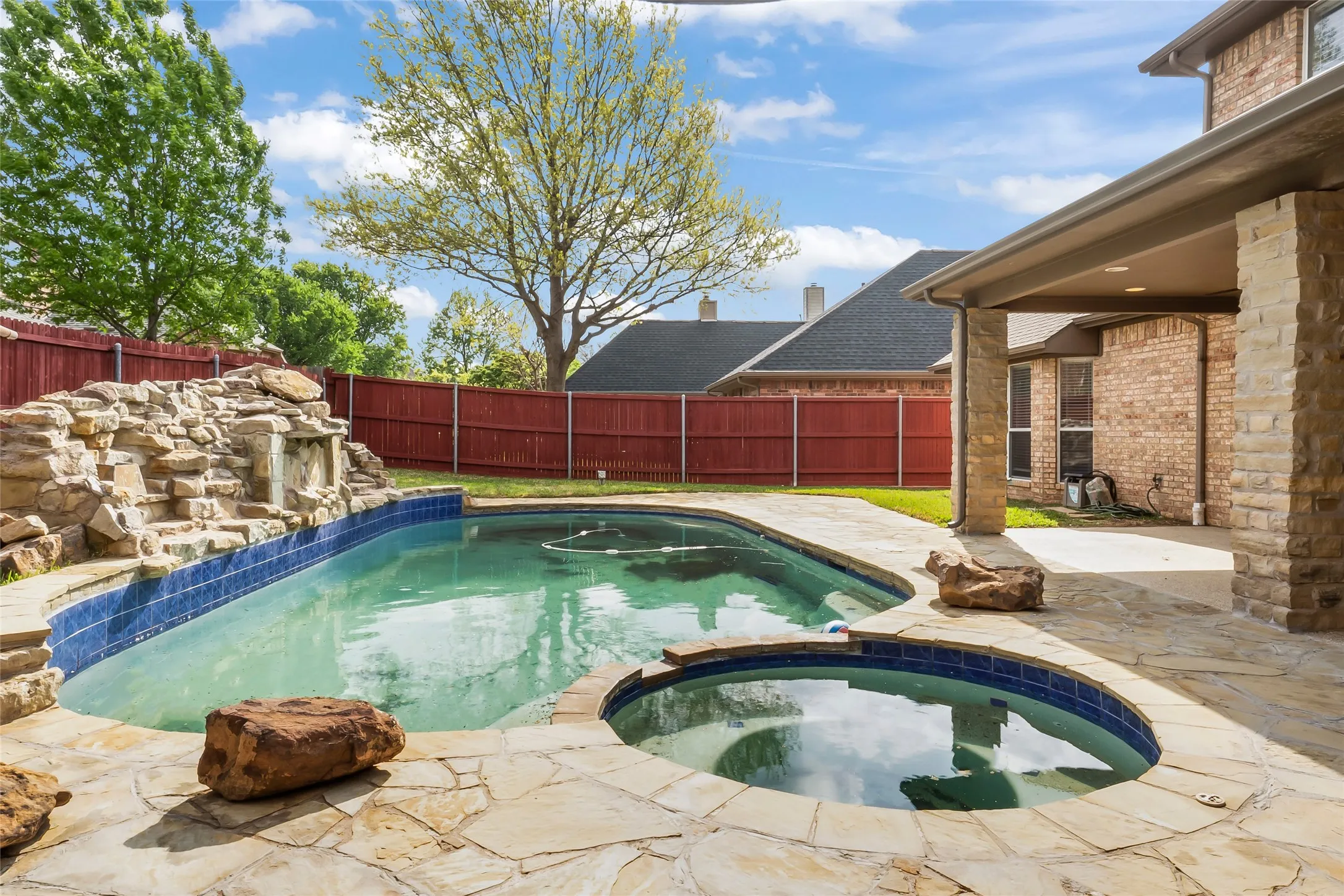 Outdoor swimming pool featuring a rock waterfall, integrated spa, and flagstone patio