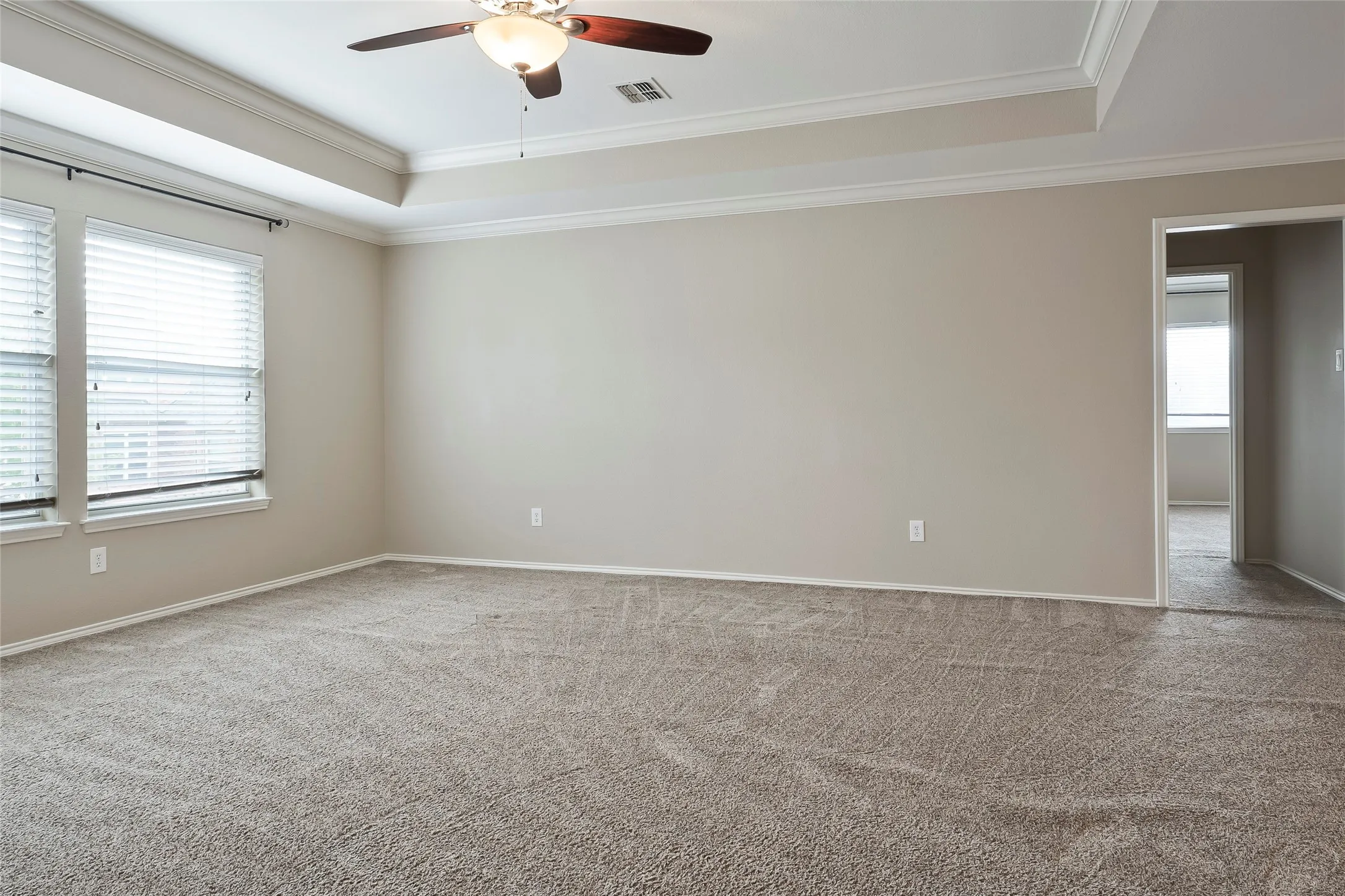 Spacious carpeted room featuring a tray ceiling with a ceiling fan, two windows with blinds, and neutral-toned walls