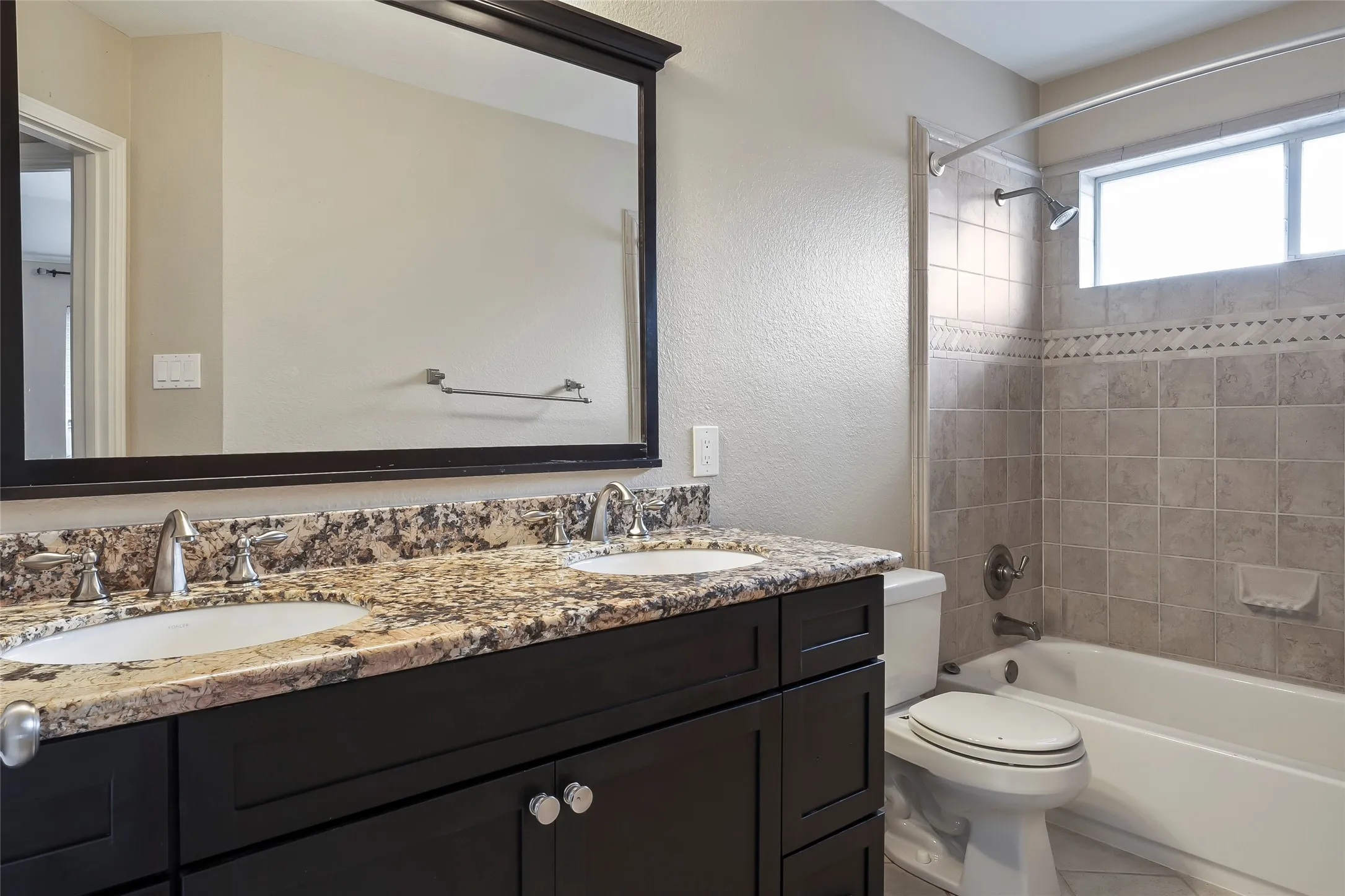 Bathroom featuring a dual-sink vanity with a granite countertop, dark wood cabinetry, and a large framed mirror