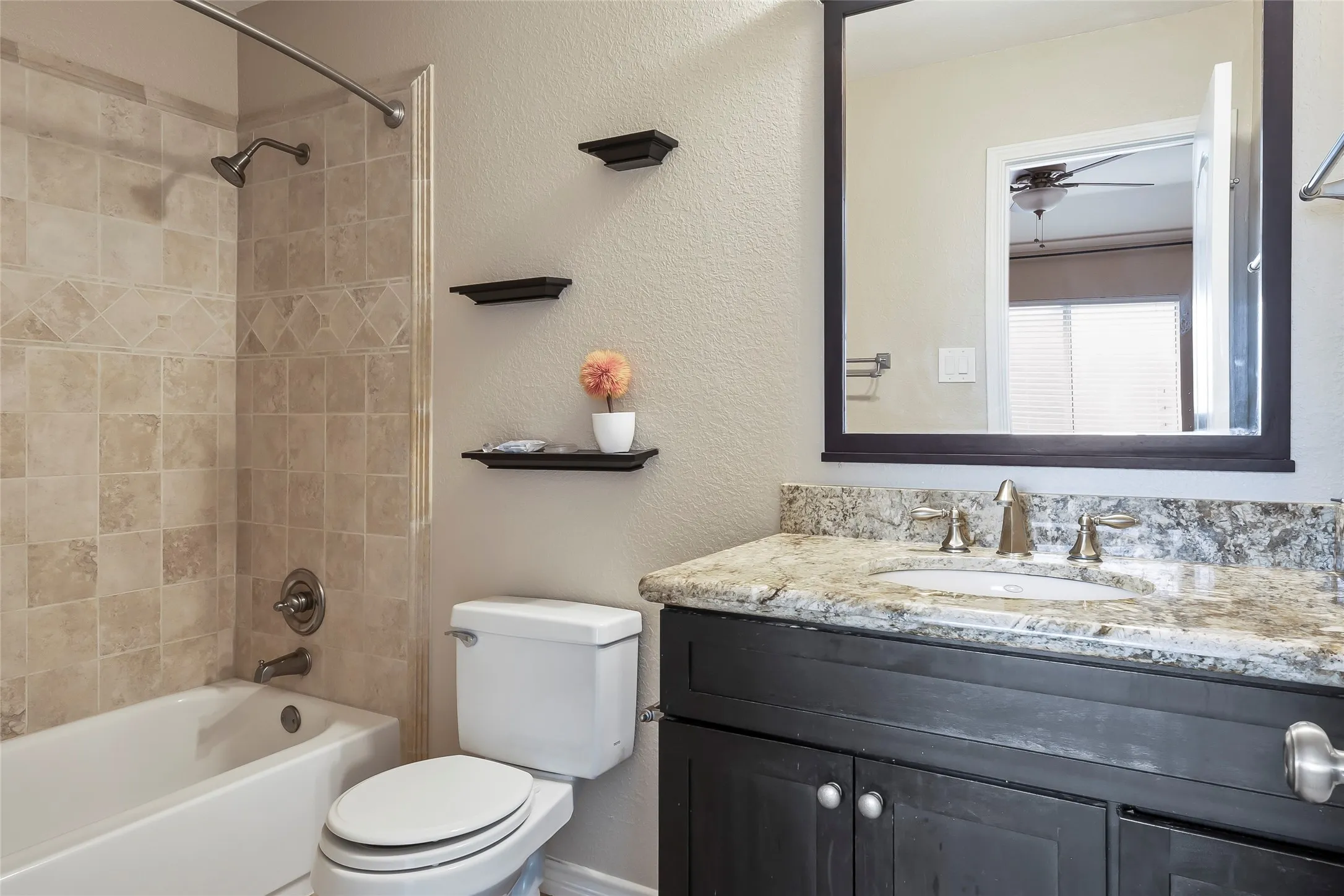Bathroom featuring a white tub, tiled shower surround, dark wood-finish vanity with a stone-look countertop, and an integrated basin with a brushed nickel faucet