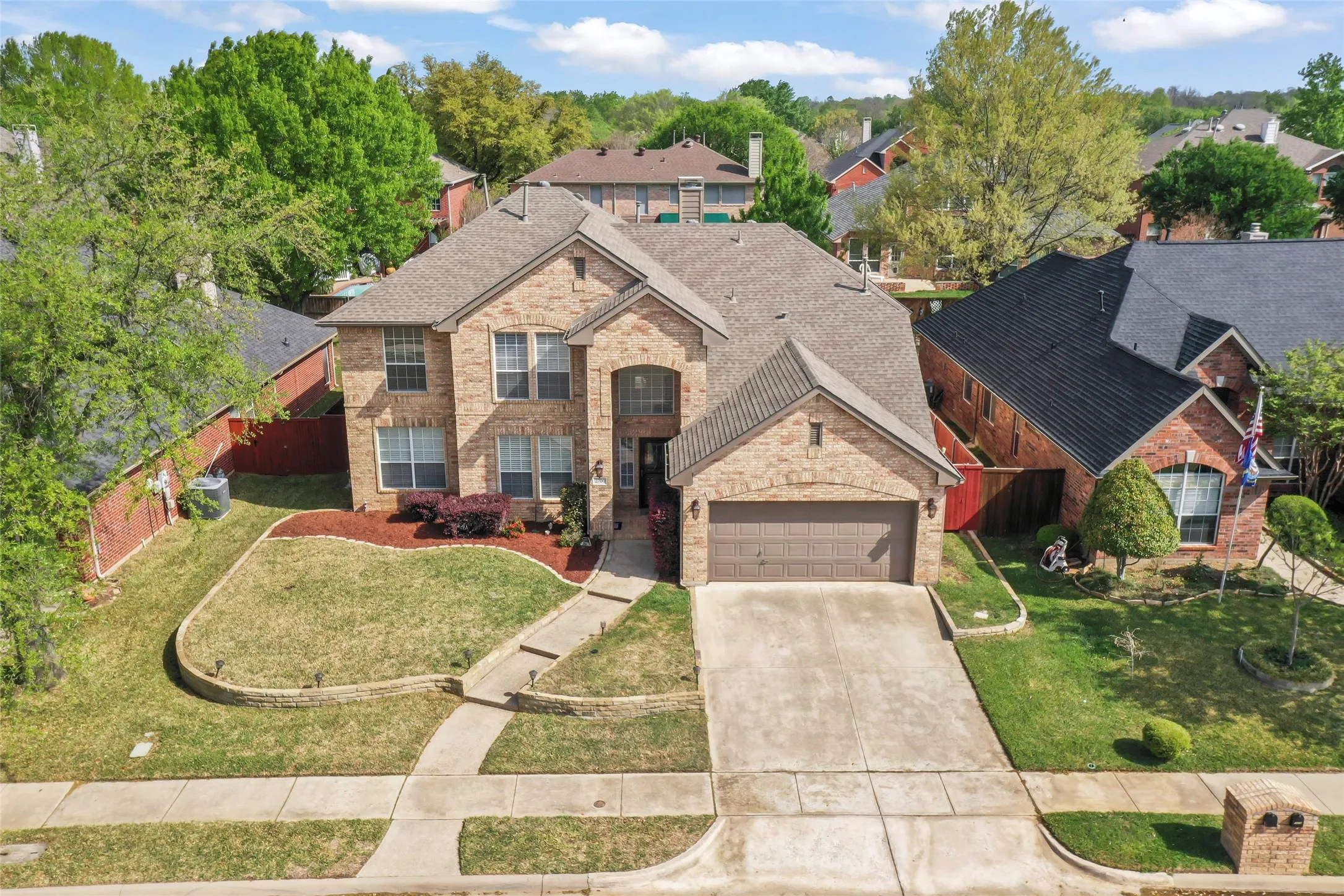 Brick exterior residence with a two-car garage, concrete driveway, and front lawn with landscaped beds