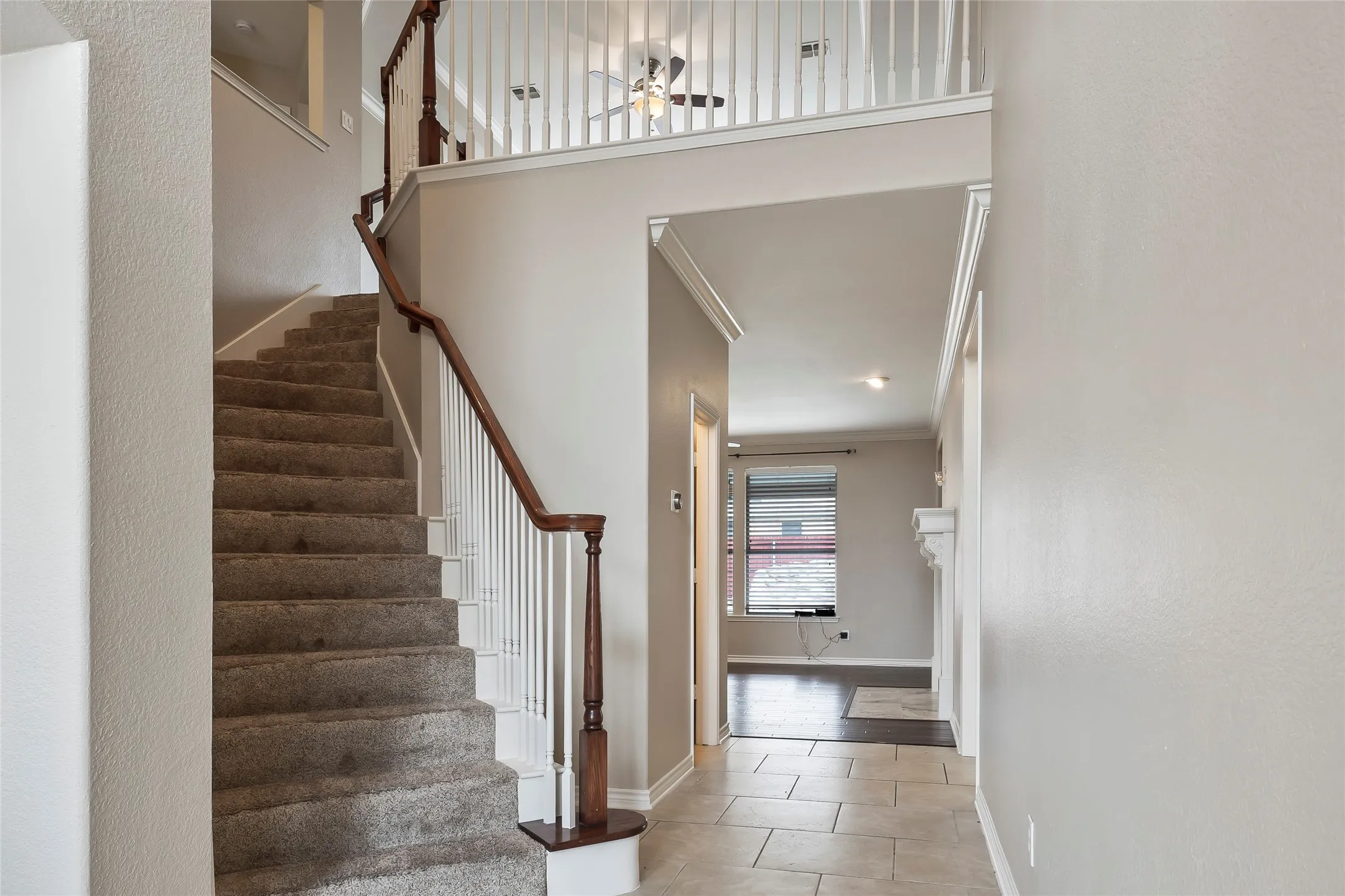 Foyer entry with tile flooring, carpeted staircase with wood handrail, white balusters, and crown molding accents