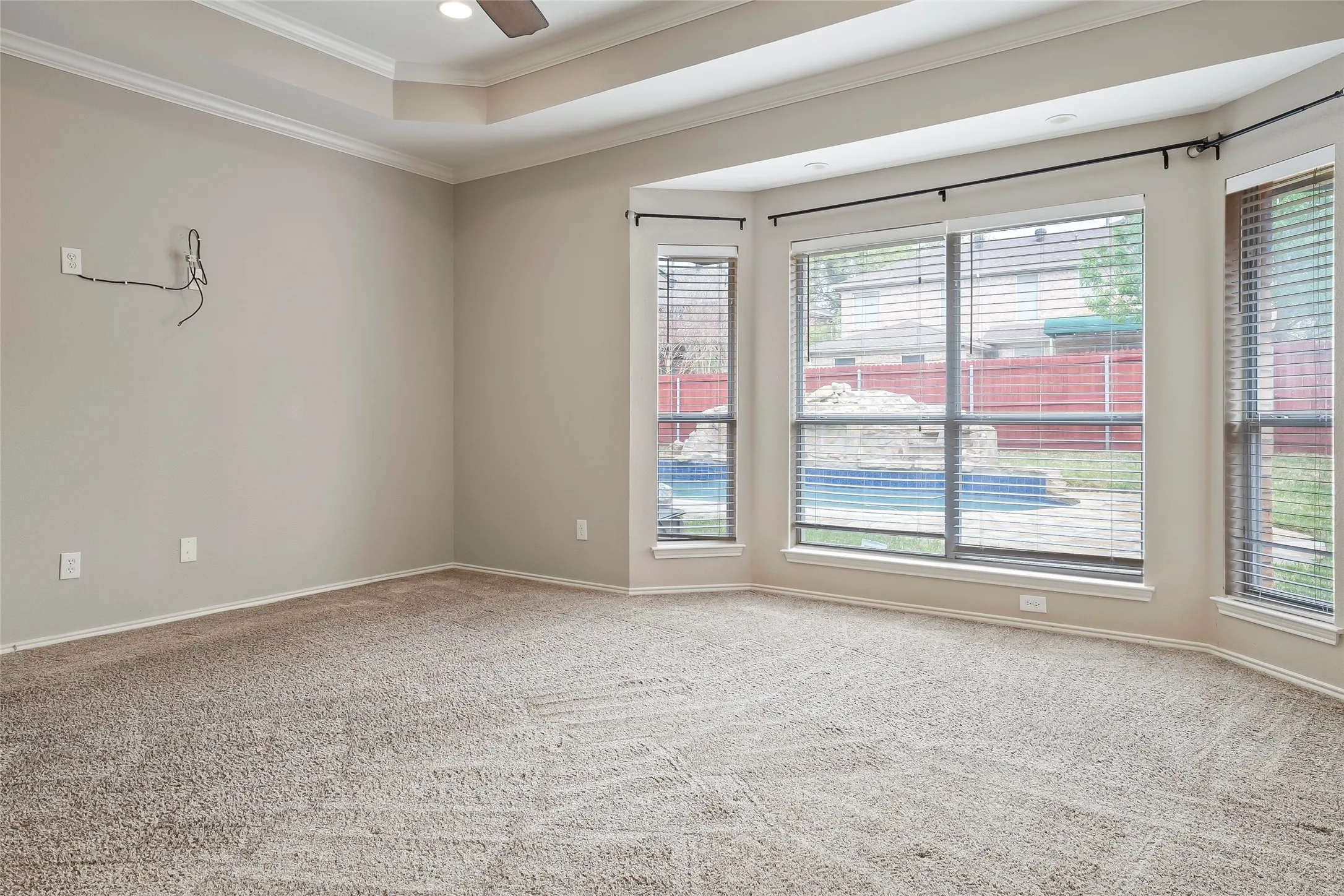Expansive room featuring a tray ceiling with a flush-mount fan, neutral carpet flooring, and a bay window configuration