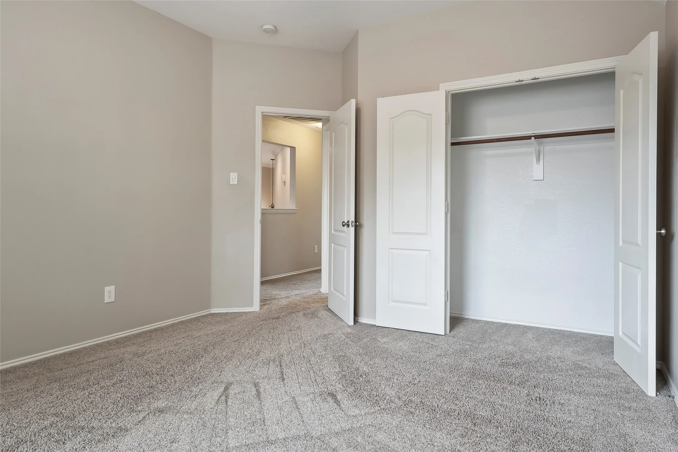 Neutral-toned room featuring a soft carpeted floor and an open closet with a hanging rod