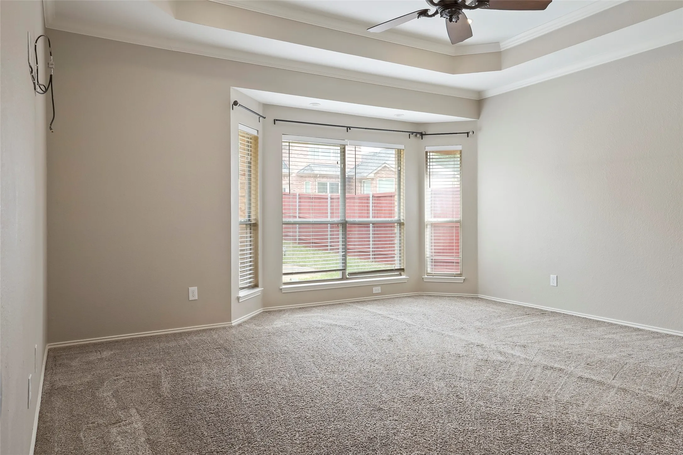 Room featuring a bay window, recessed tray ceiling, and a ceiling fan