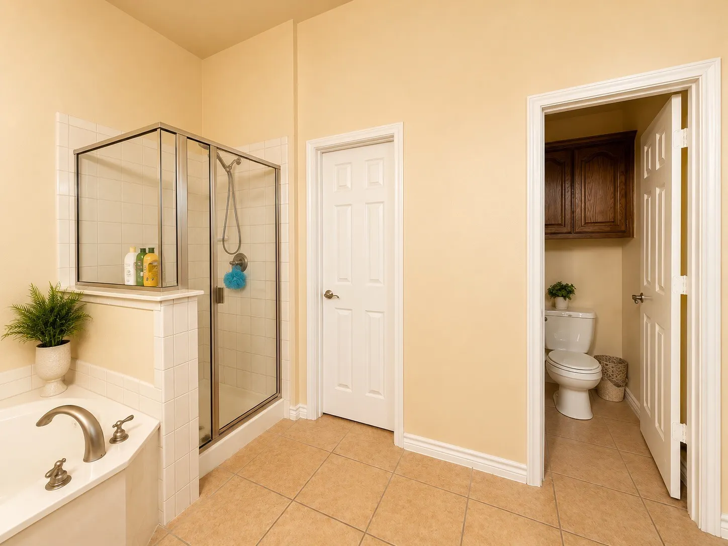 Ceramic tile flooring, built-in bathtub, glass-enclosed shower, white interior doors, and wood-finish cabinetry