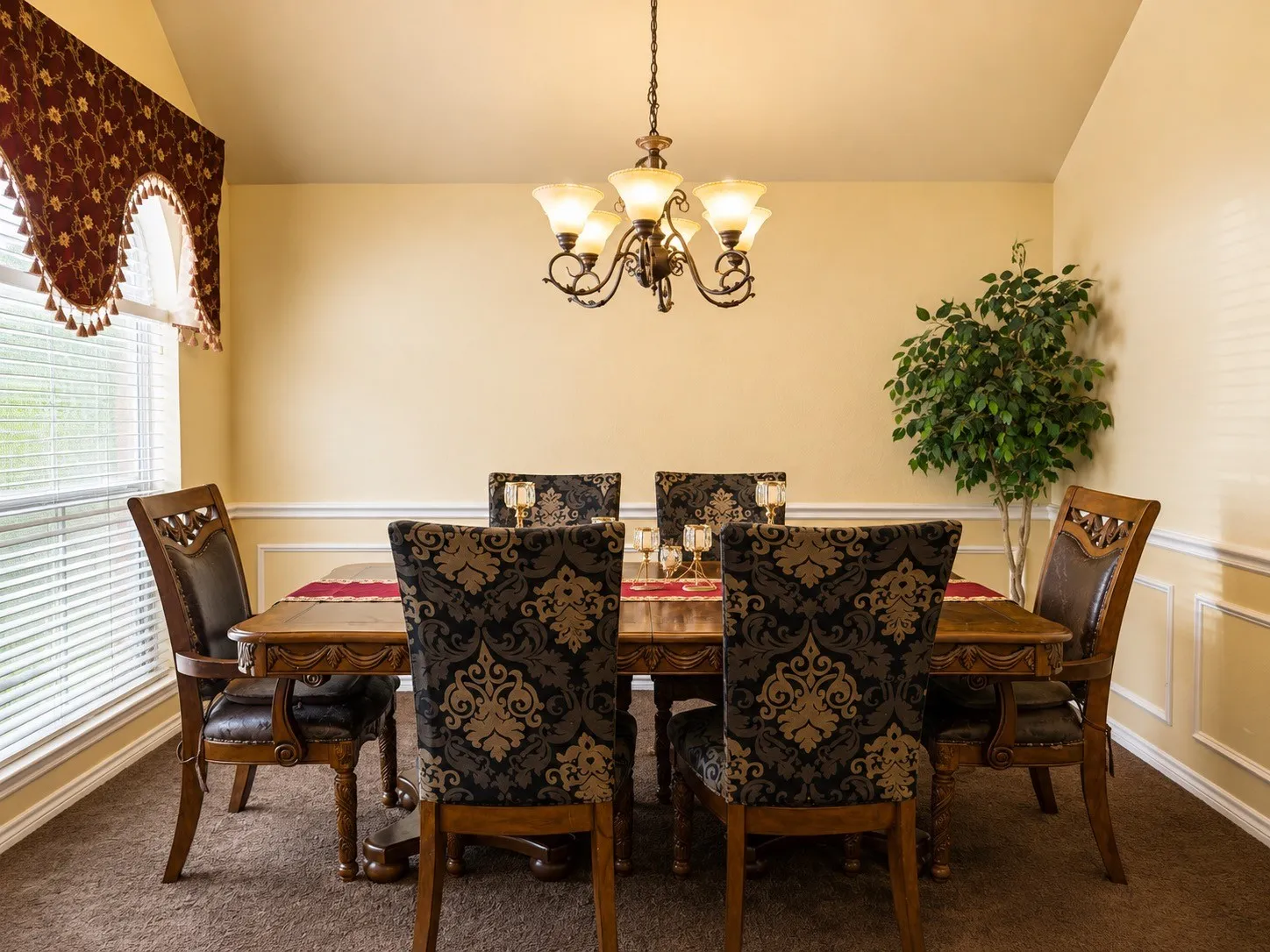 Angled ceiling, decorative wall molding, window blinds, wood-finish dining table, and an ornamental chandelier