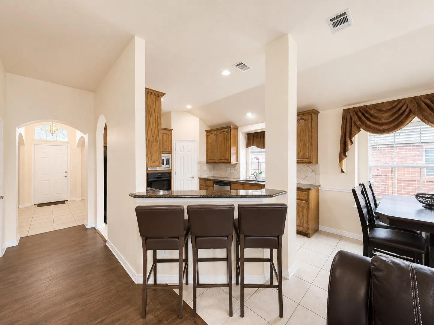 Open-concept kitchen and dining area featuring a large center island with seating for three, wood-finish flooring throughout, white cabinetry with wood accents, stainless steel appliances, and recessed lighting