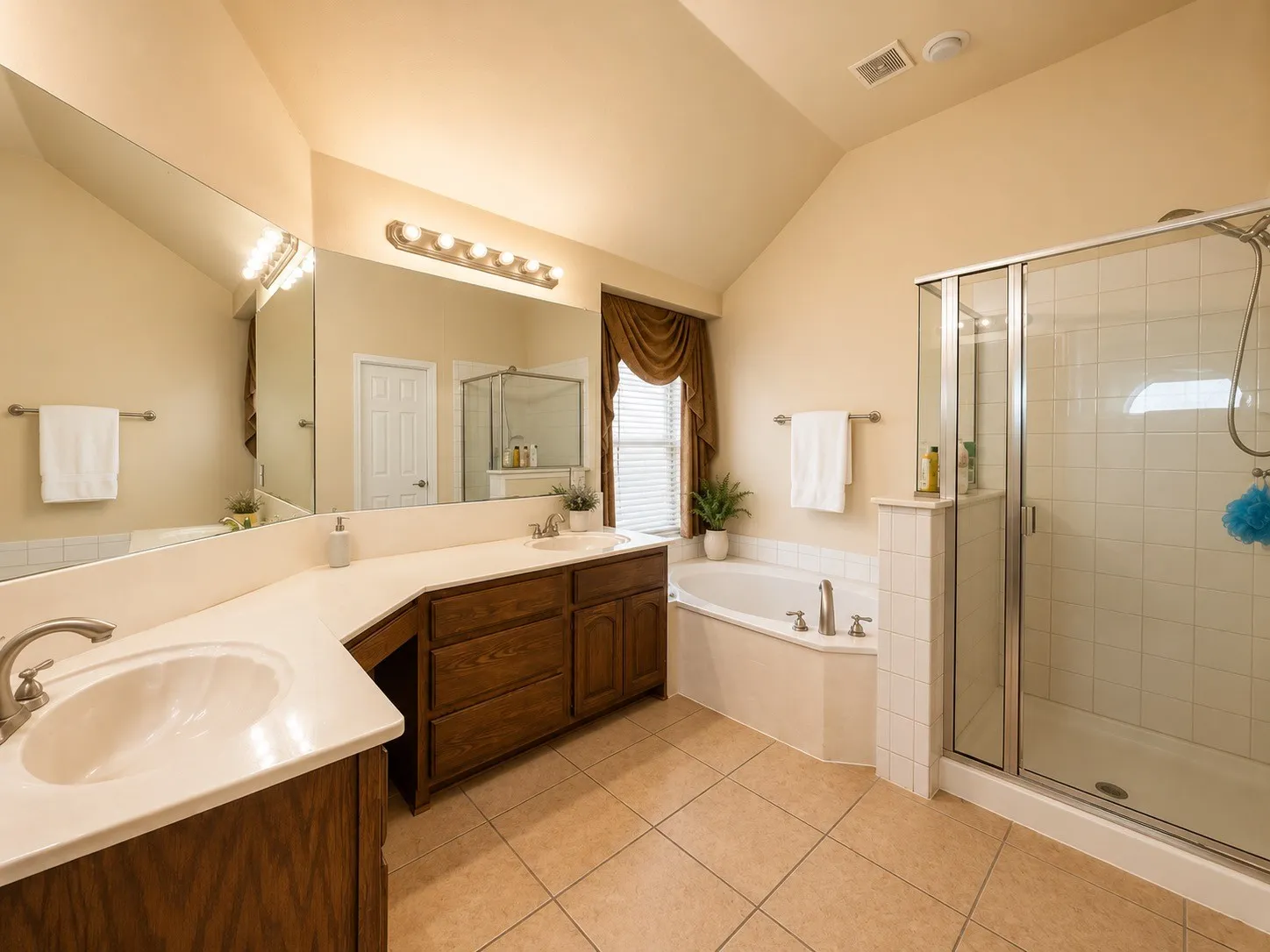 Spa-inspired primary bathroom featuring dual vanities with wood cabinetry, ceramic tile flooring, and abundant natural lighting from multiple windows