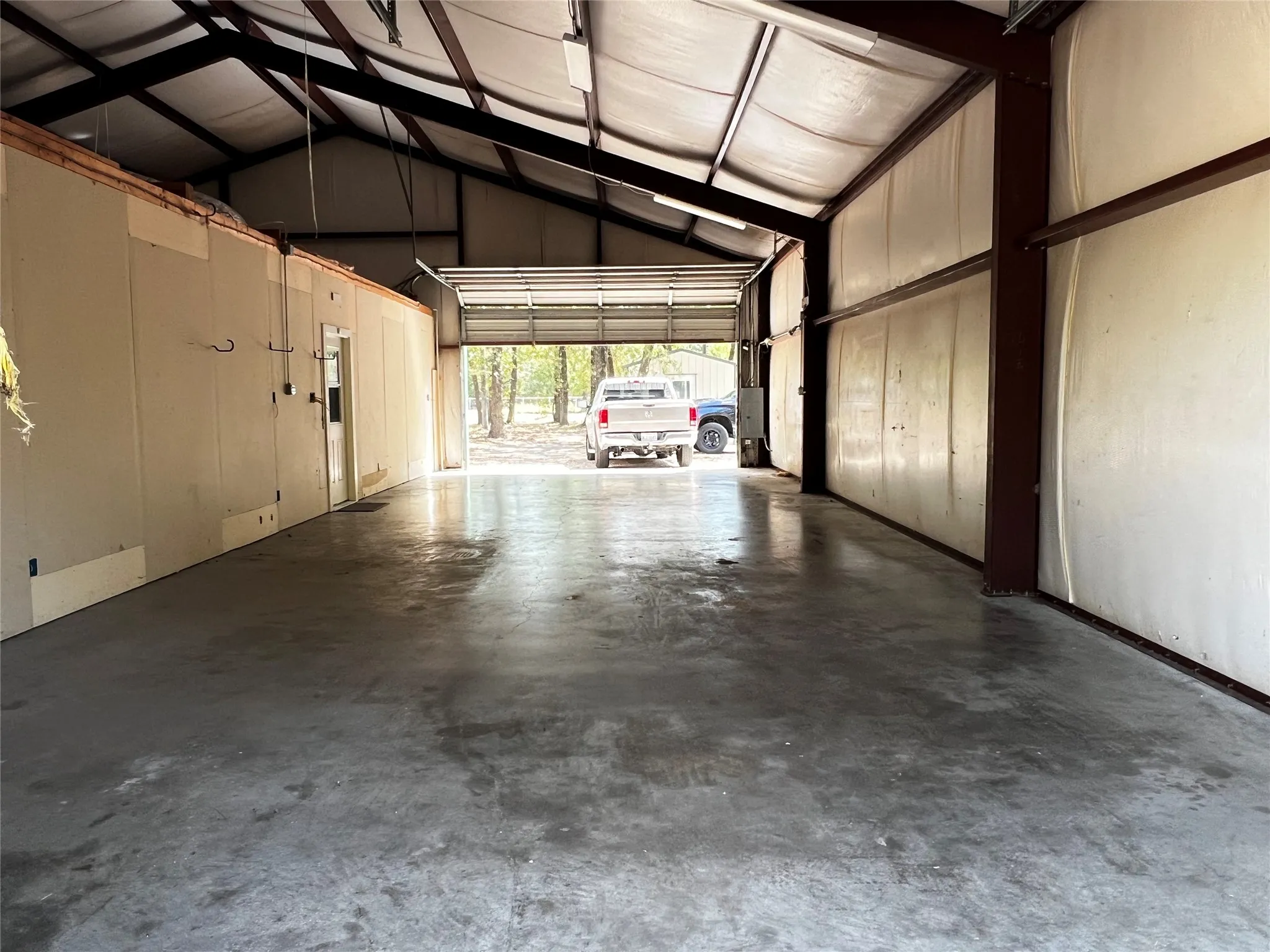 Garage - Workshop - Expansive open interior with concrete flooring, insulation, exposed structural beams, 12' eave height and 10' high roll-up double south end garage door.  Looking from from north end roll-up garage door.