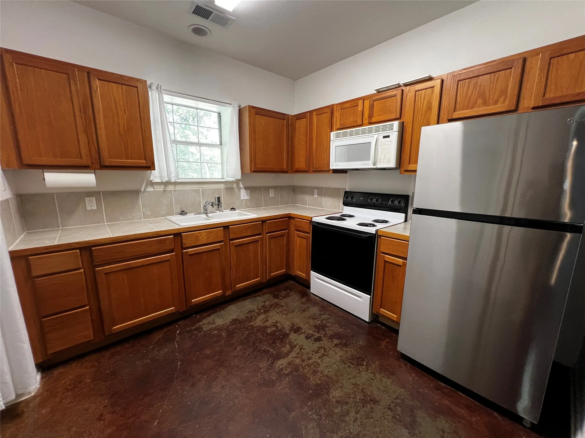 Kitchen featuring wood cabinetry, tile countertops, stainless steel refrigerator, white electric range, and a built-in microwave